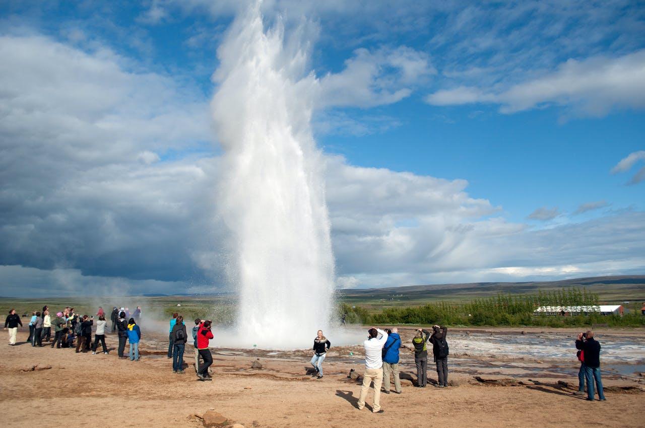 Strokkur hot spring sporuting a jet of hot water in the air at the Geysir geothermal area in Iceland with some people wathcing