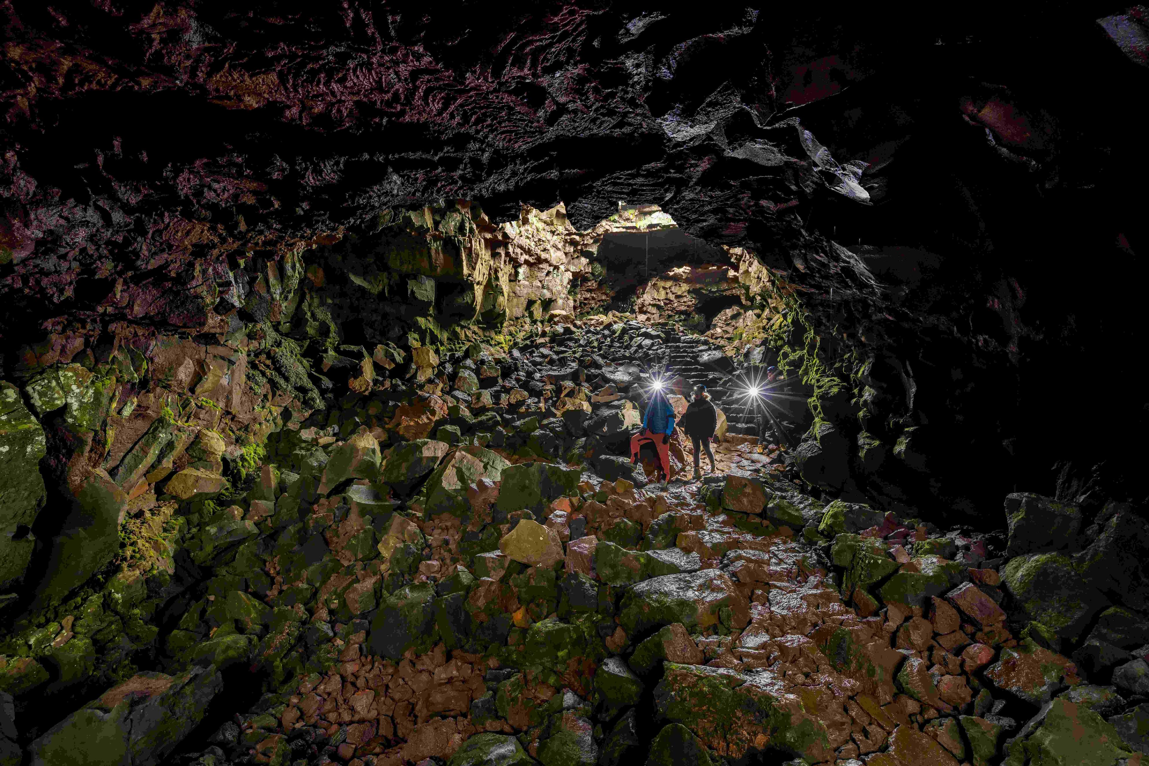 Three people with headlamps exploring the wide section of Raufarhólshellir lava tunnel.