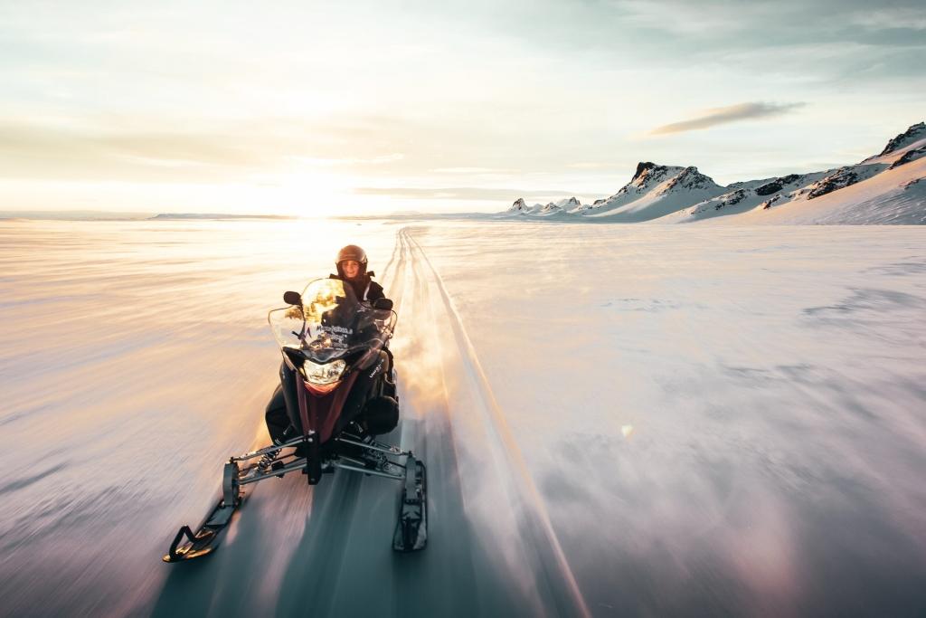 A solo snowmobiler racing at sunset with a dramatic sky backdrop.