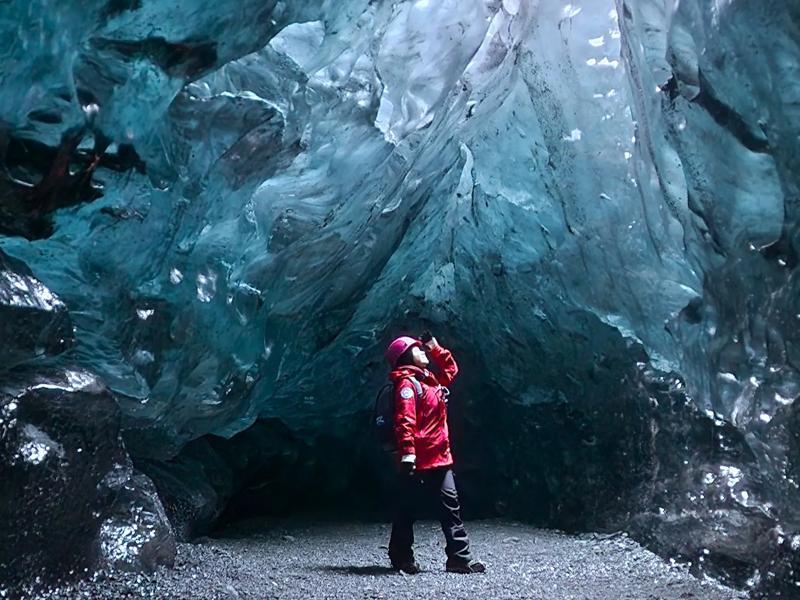 A guide with a helmet standing inside an ice cave and looking up