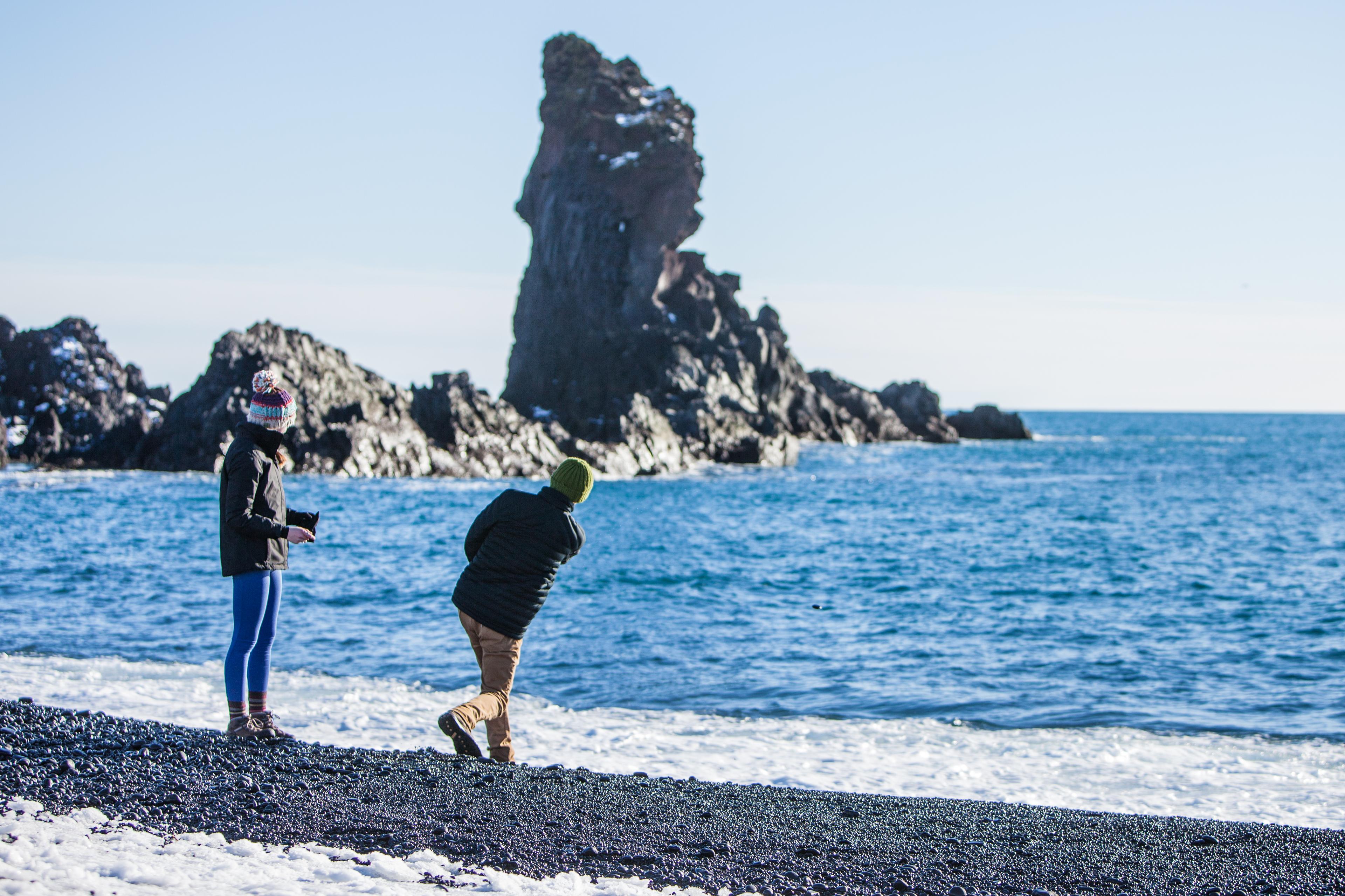 A man throwing a rock into the ocean at Djúpalónssandur black beach