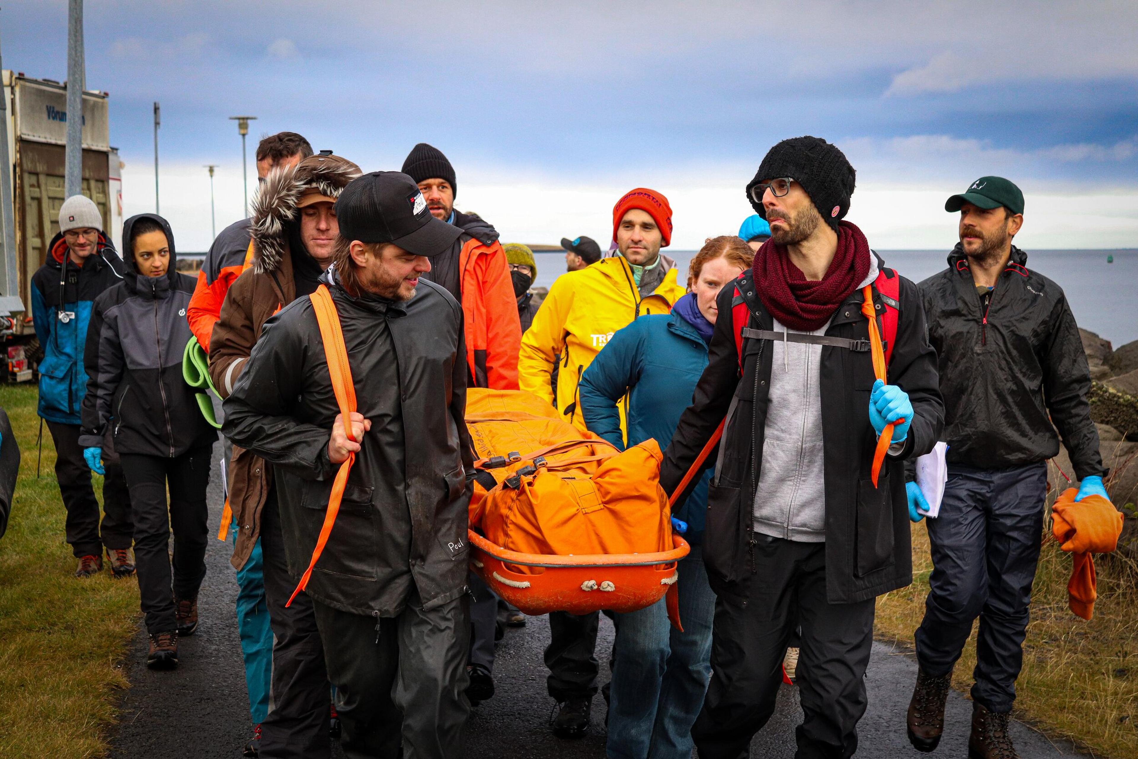 a group of people engaged in a simulated rescue exercise, carrying a stretcher with an orange cover in an outdoor setting