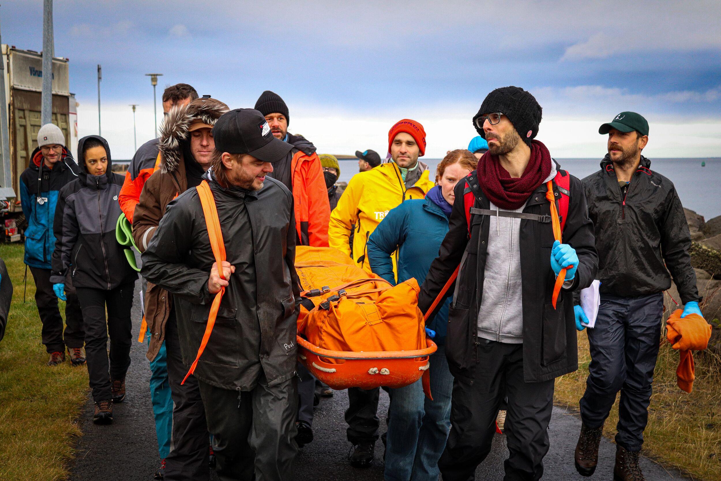 A group of Wilderness First Responder course participants carry a stretcher in a team exercise, simulating a rescue scenario.
