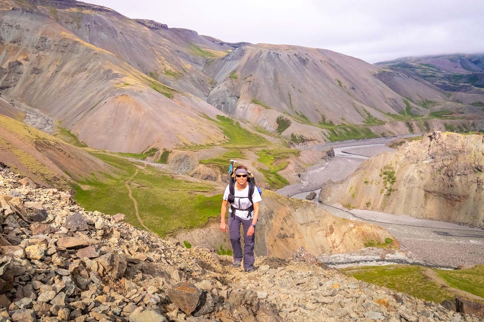 A hiker ascending up a slope leading from a valley with a river flowing through