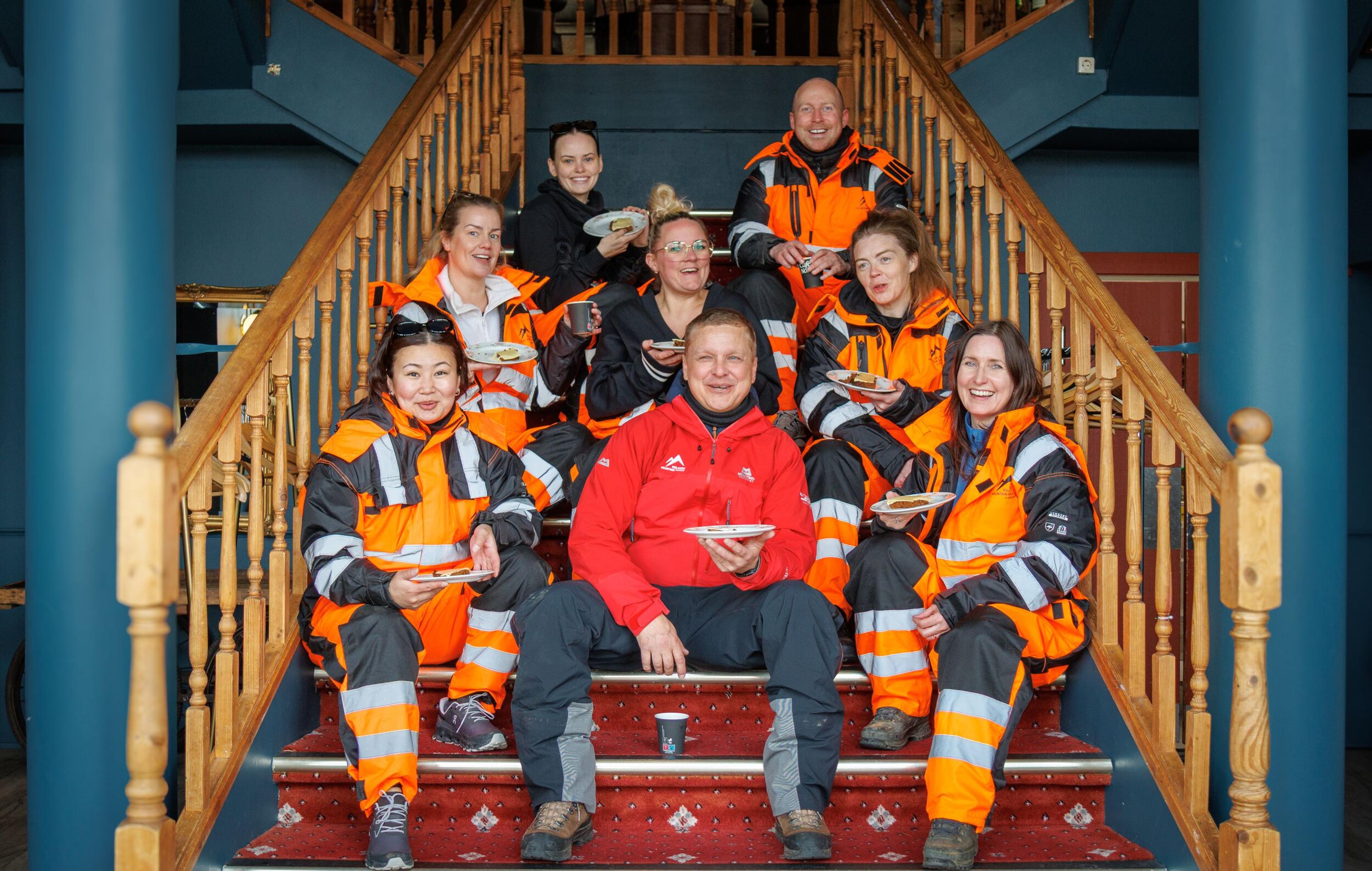 Group of people sitting on a staircase, holding plates and smiling at the camera.