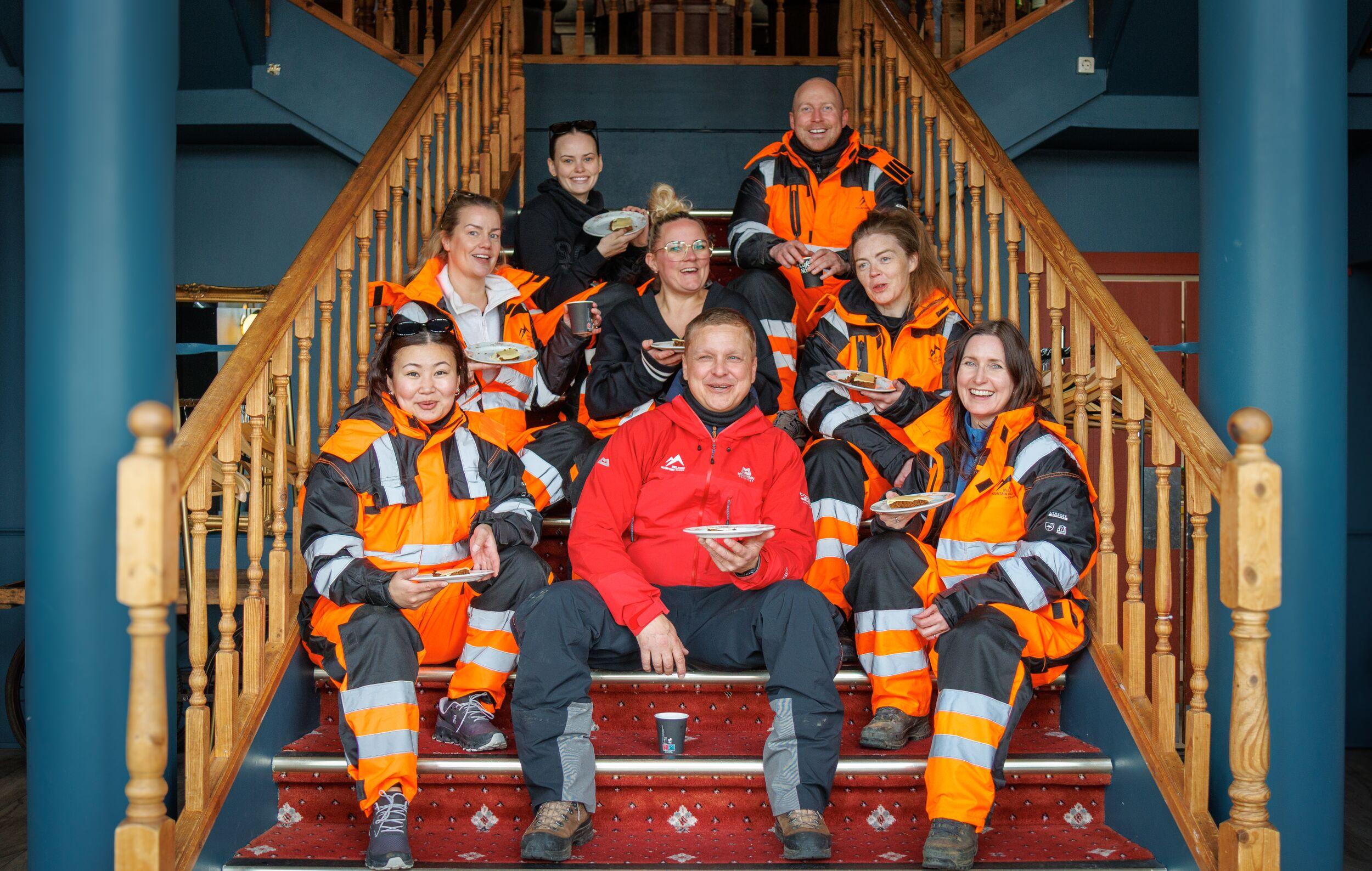 Group of people sitting on a staircase, holding plates and smiling at the camera.
