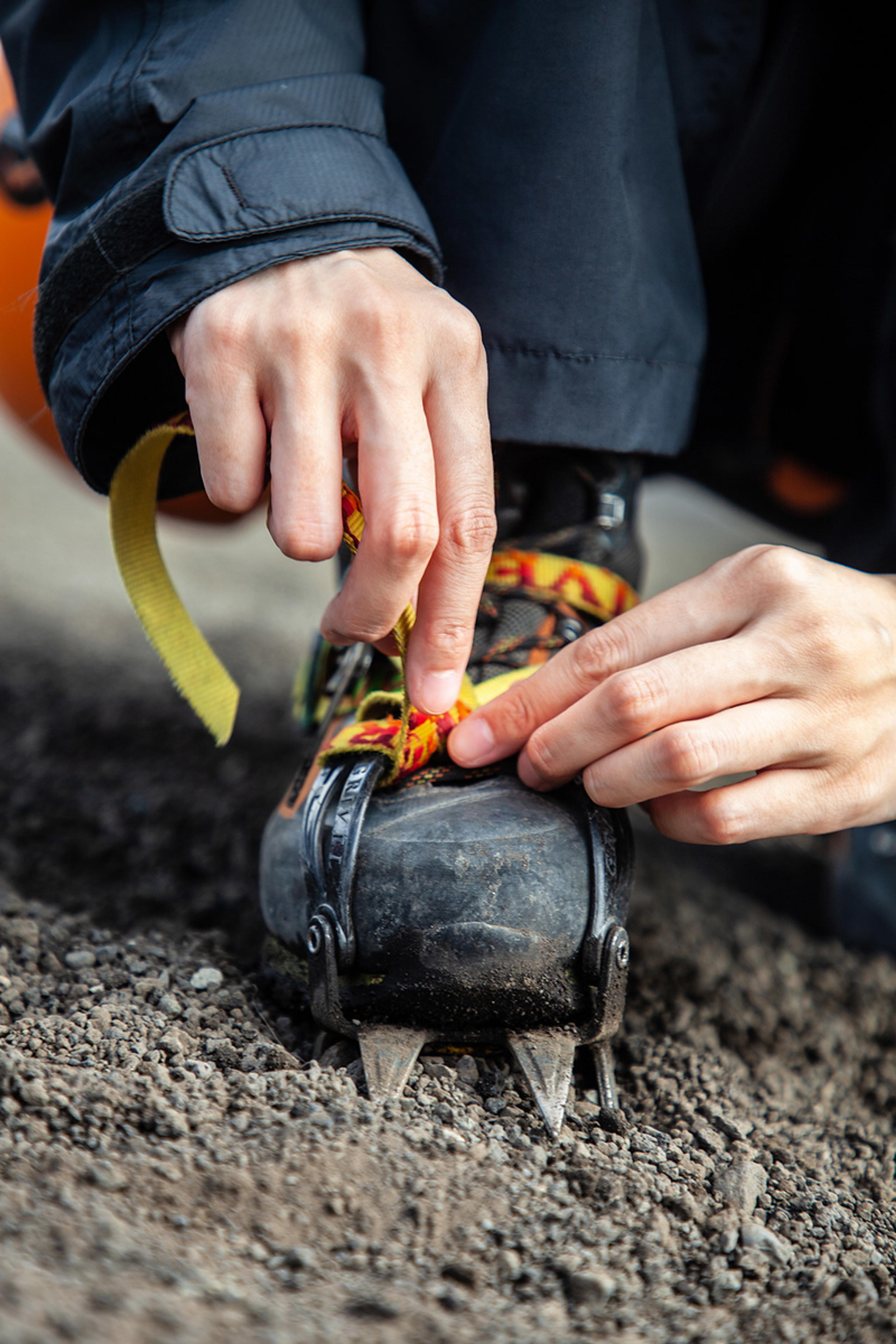 Hands tying the strings to fasten the crampons on the boots