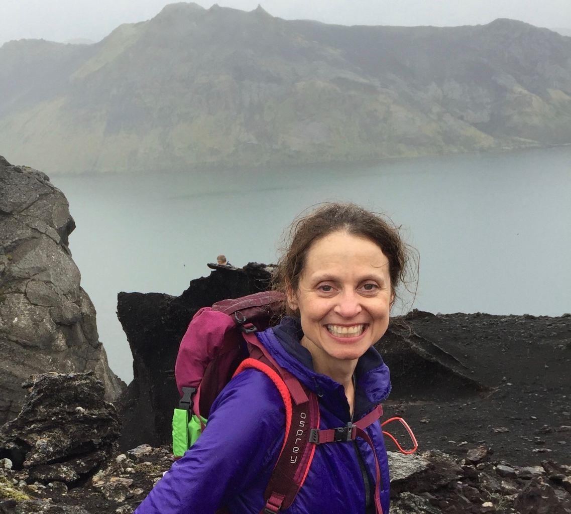 A picture of a hiking woman with the sea and mountains in the back