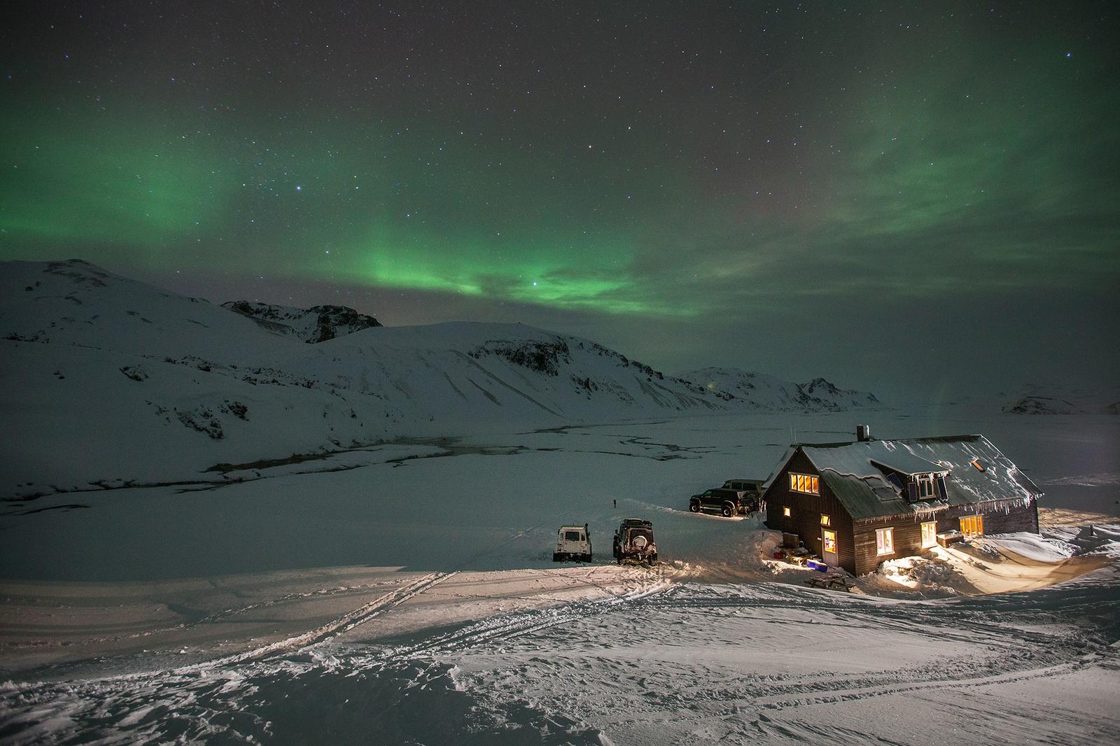 Cozy hut covered in snow with snowy mountains in backgrond with northen lights shining over them