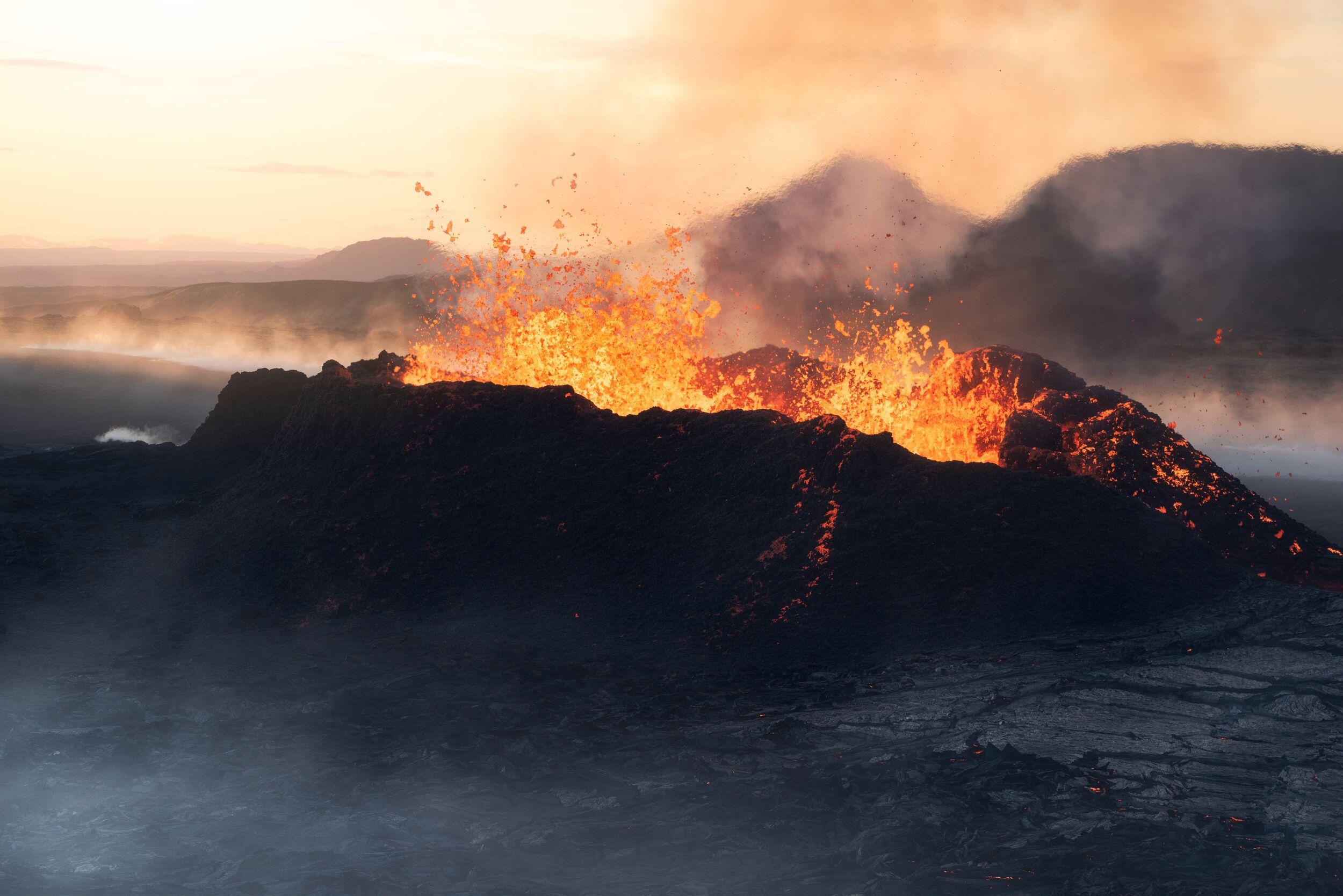 Flaming red lava erupting from a crater at sunset