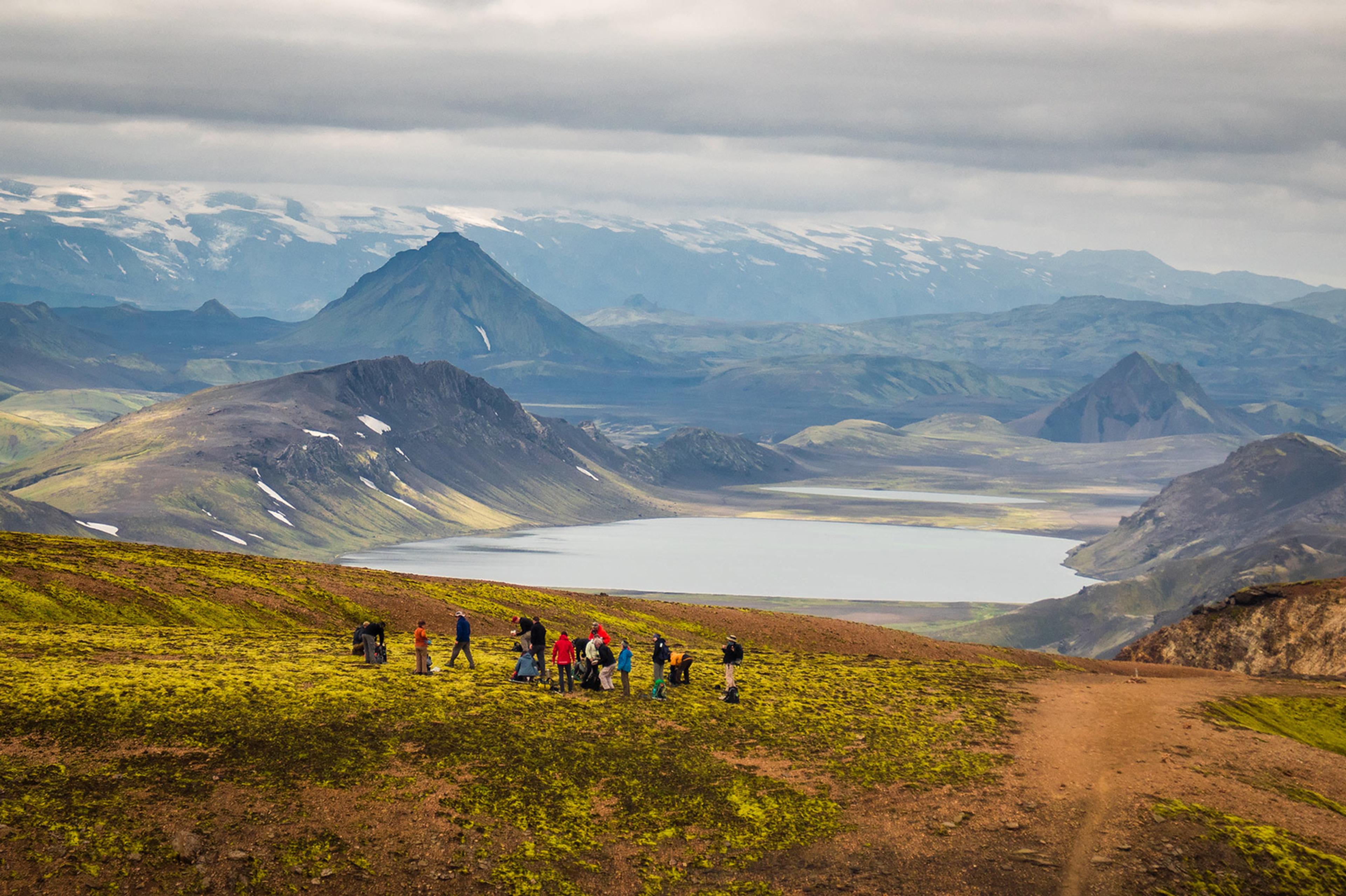 A few explorers enjoying the scenery of the lake and colorful mountains on the soft moss