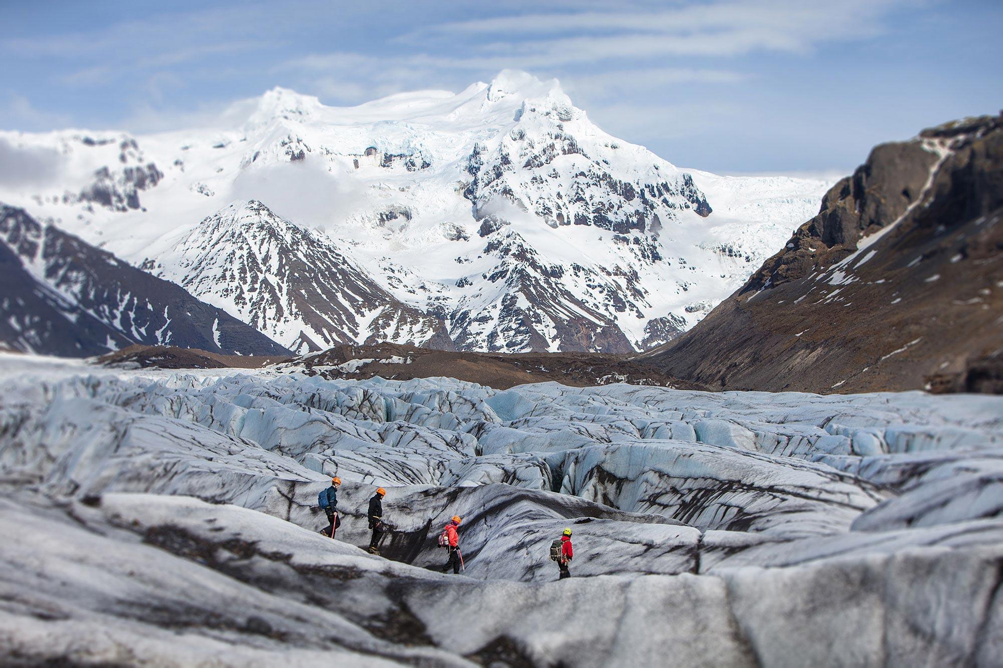 People on a Glacier Walk in Iceland with snow covered mountains behind them.