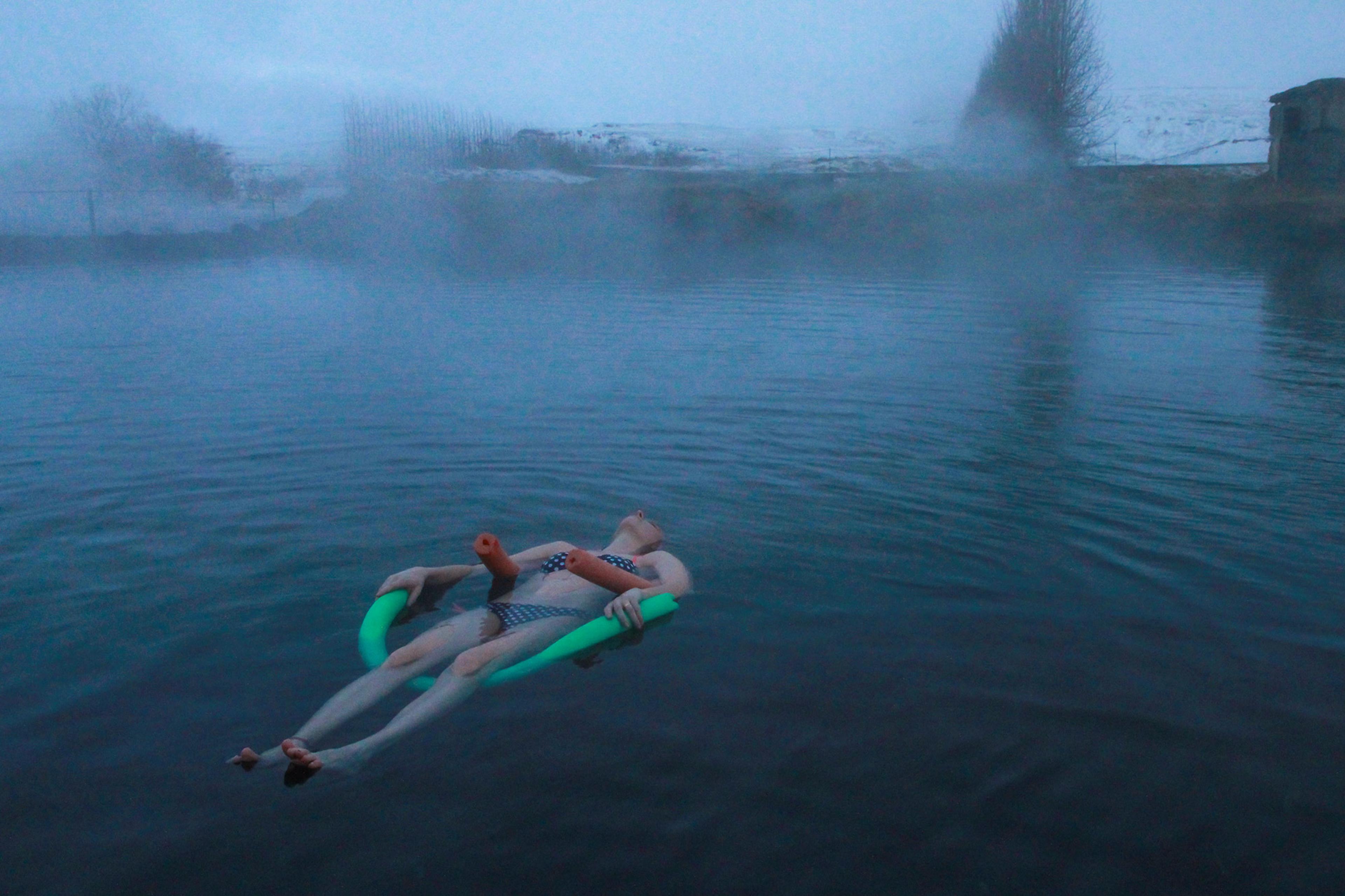 A woman floating on the surfice of a natural thermal bath in Iceland in April