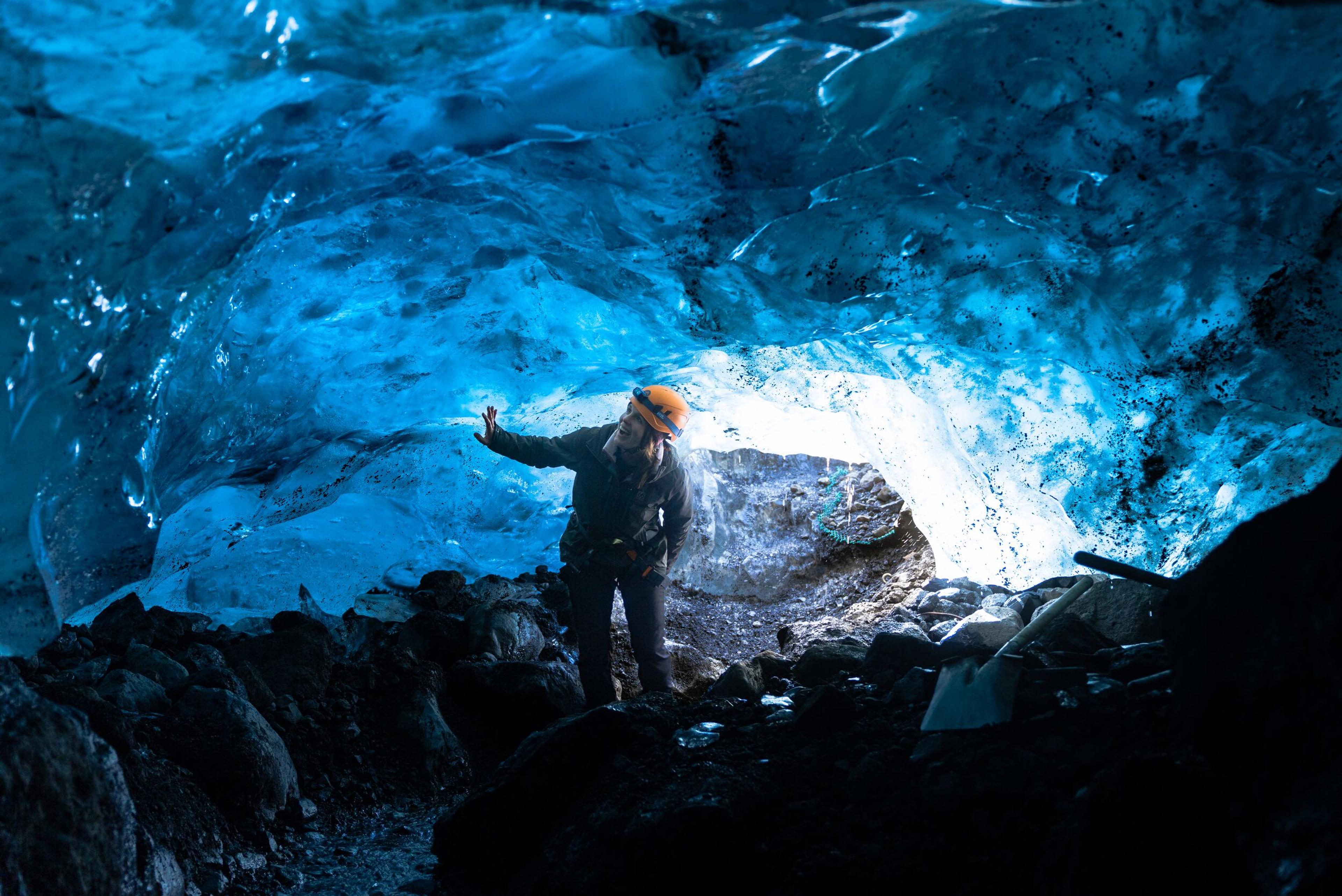 Person standing in a blue ice cave with a hand on the ice