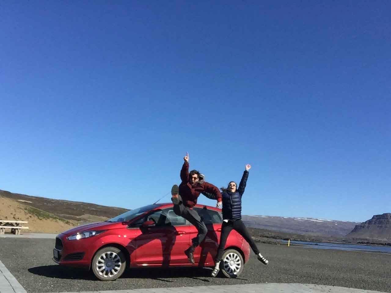 Jumping of Joy in front of a red car on a sunny day