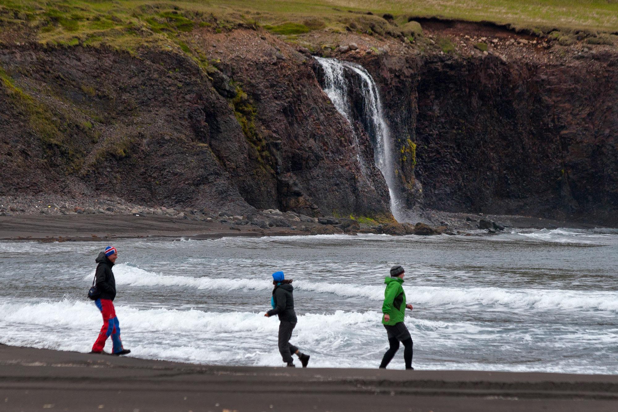 People having fun at a black sand beach by a waterfall