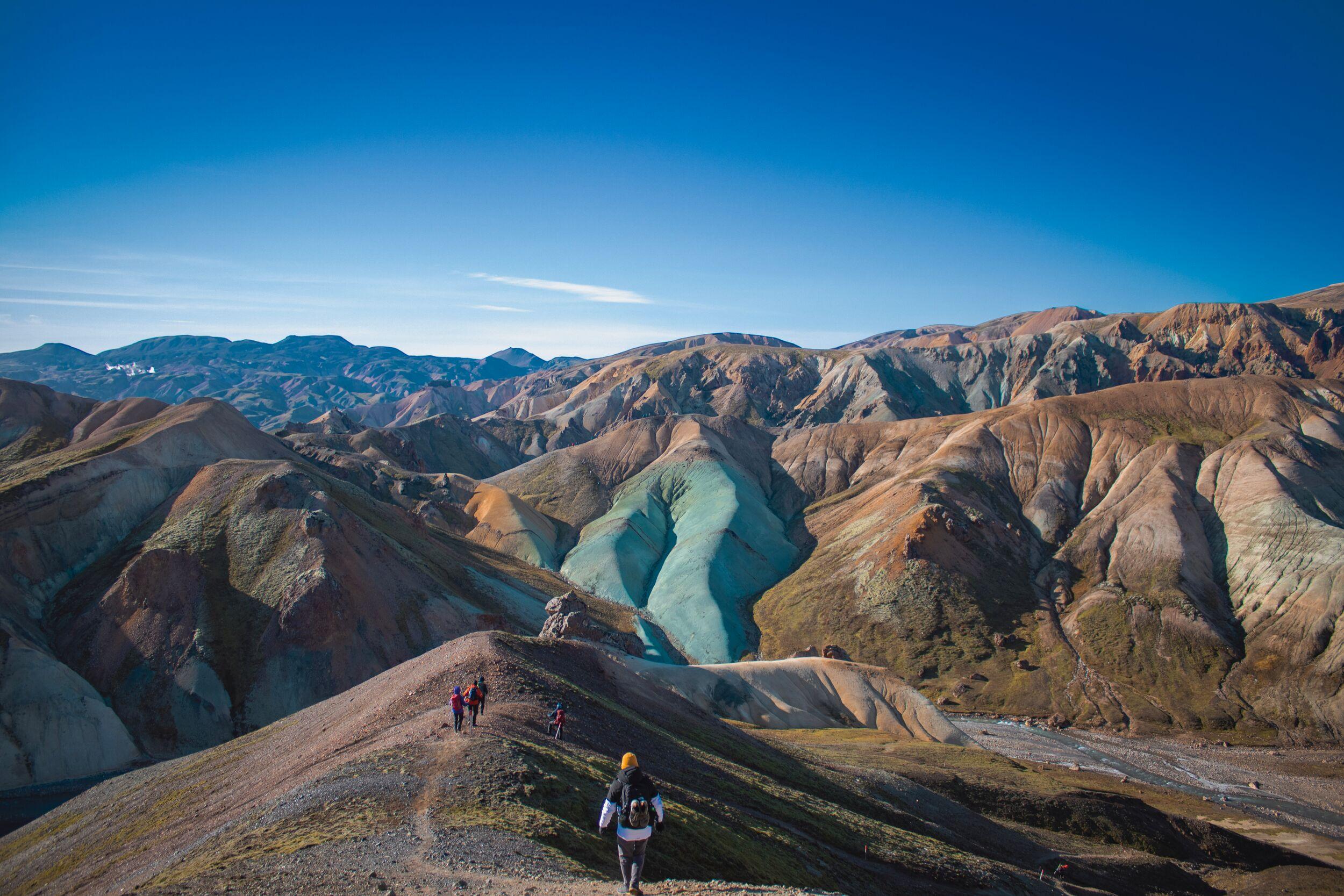 A striking green ridge stands out against the earthy tones of the surrounding mountains in Landmannalaugar, with a rocky valley and clear skies completing the scenic view.