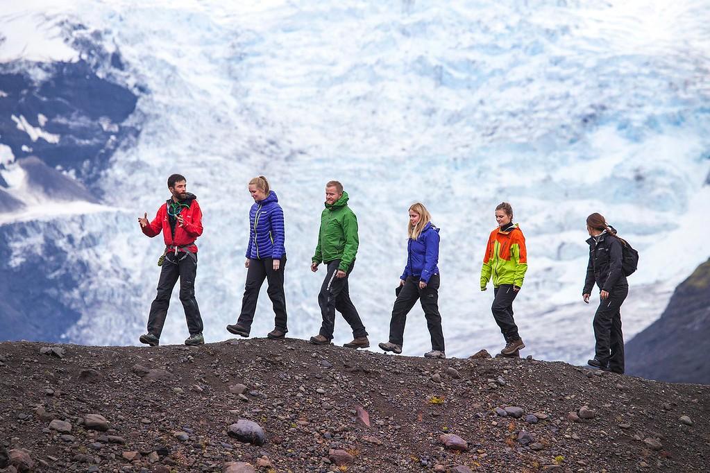 people hiking and listening to their guide with a glacier in the back.