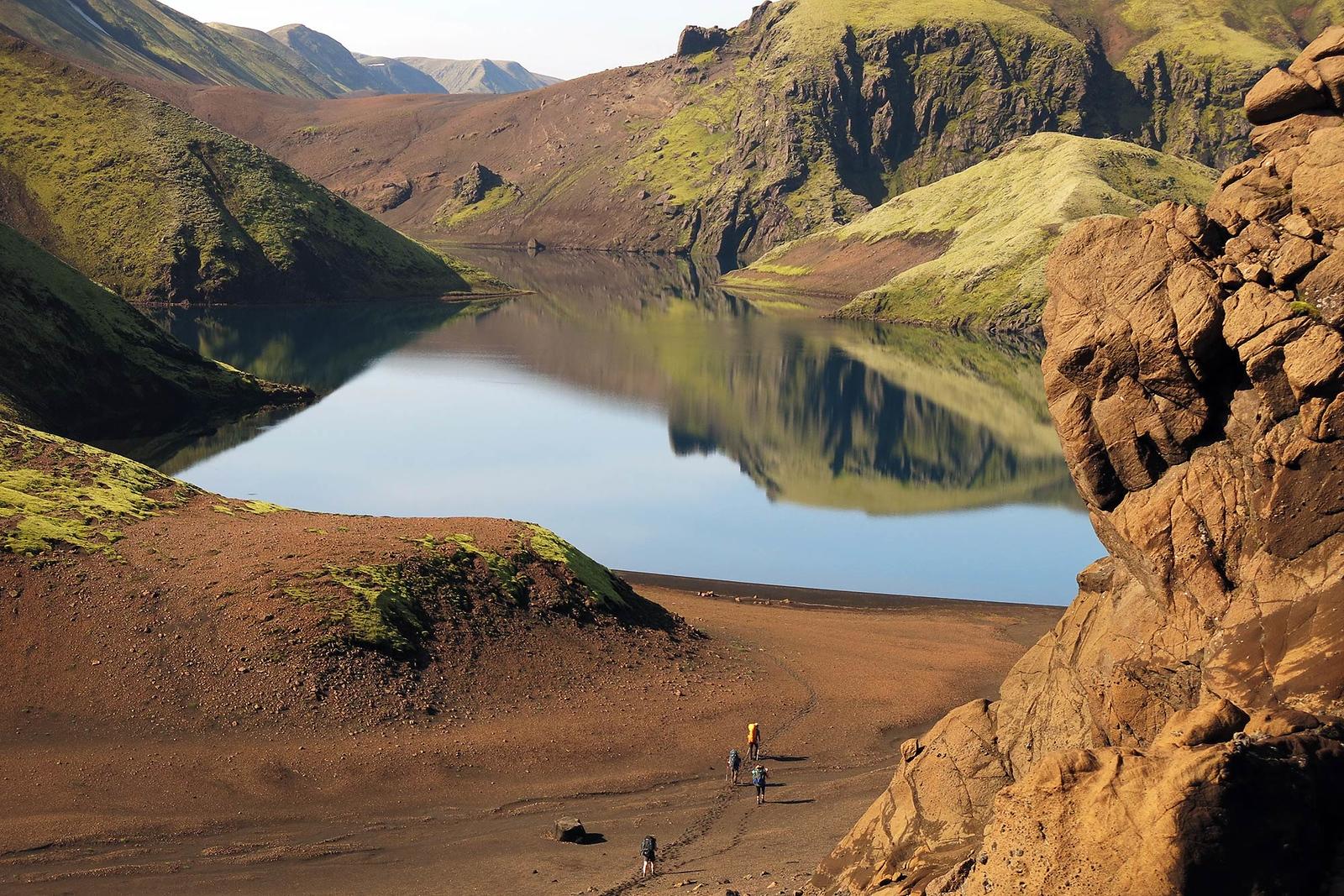 People walking to a big beautiful water surrounded by mossy hills during a sunny day