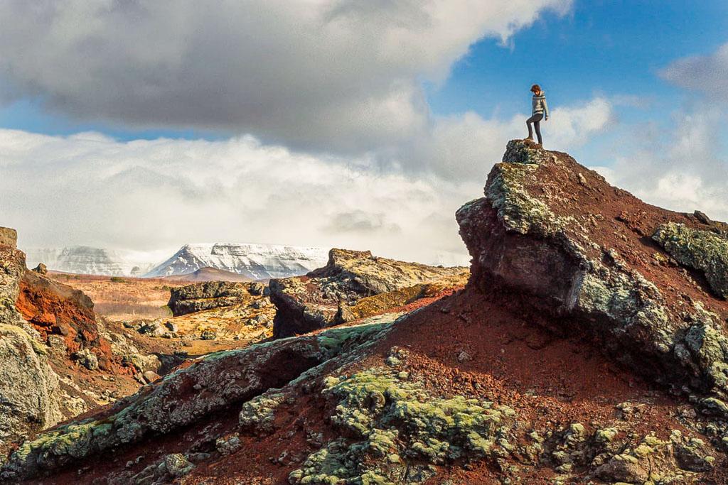 A female wearing traditional Icelandic sweater standing on the top of a red rock