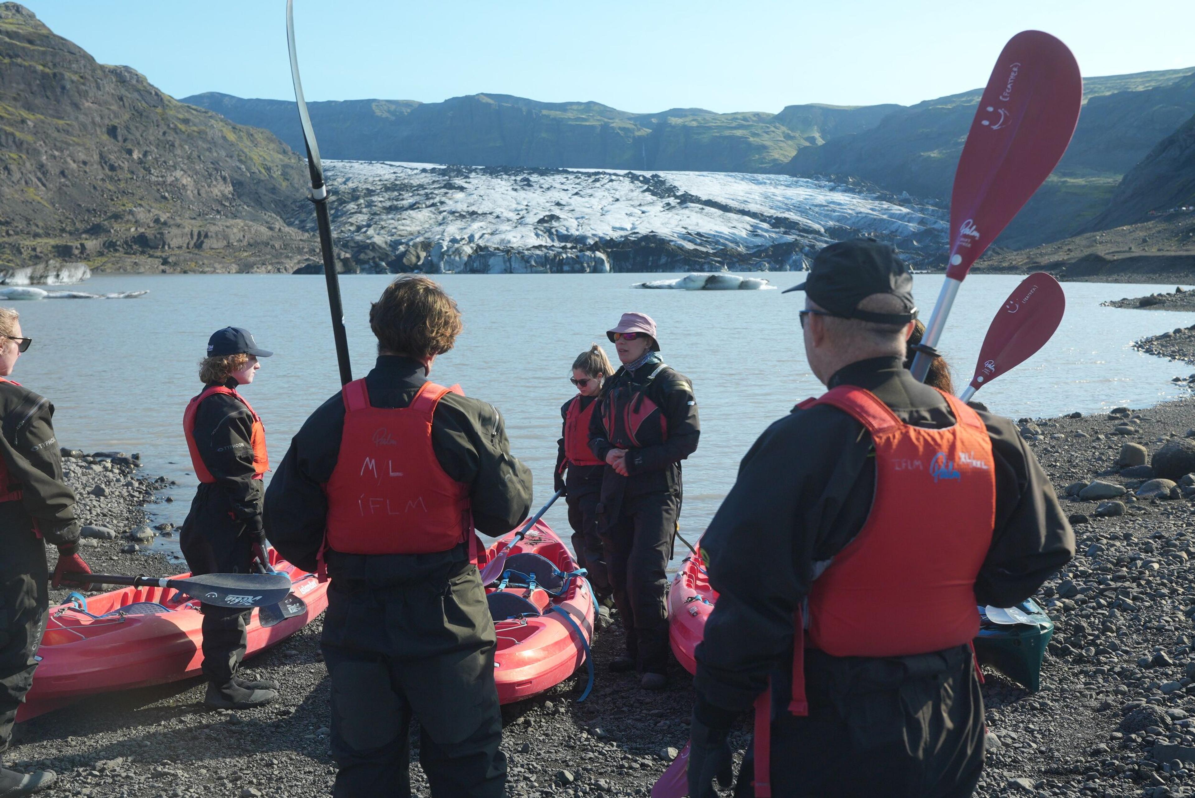 A group of people in red life jackets about to embark on a kayak excursion on a glacier lagoon
