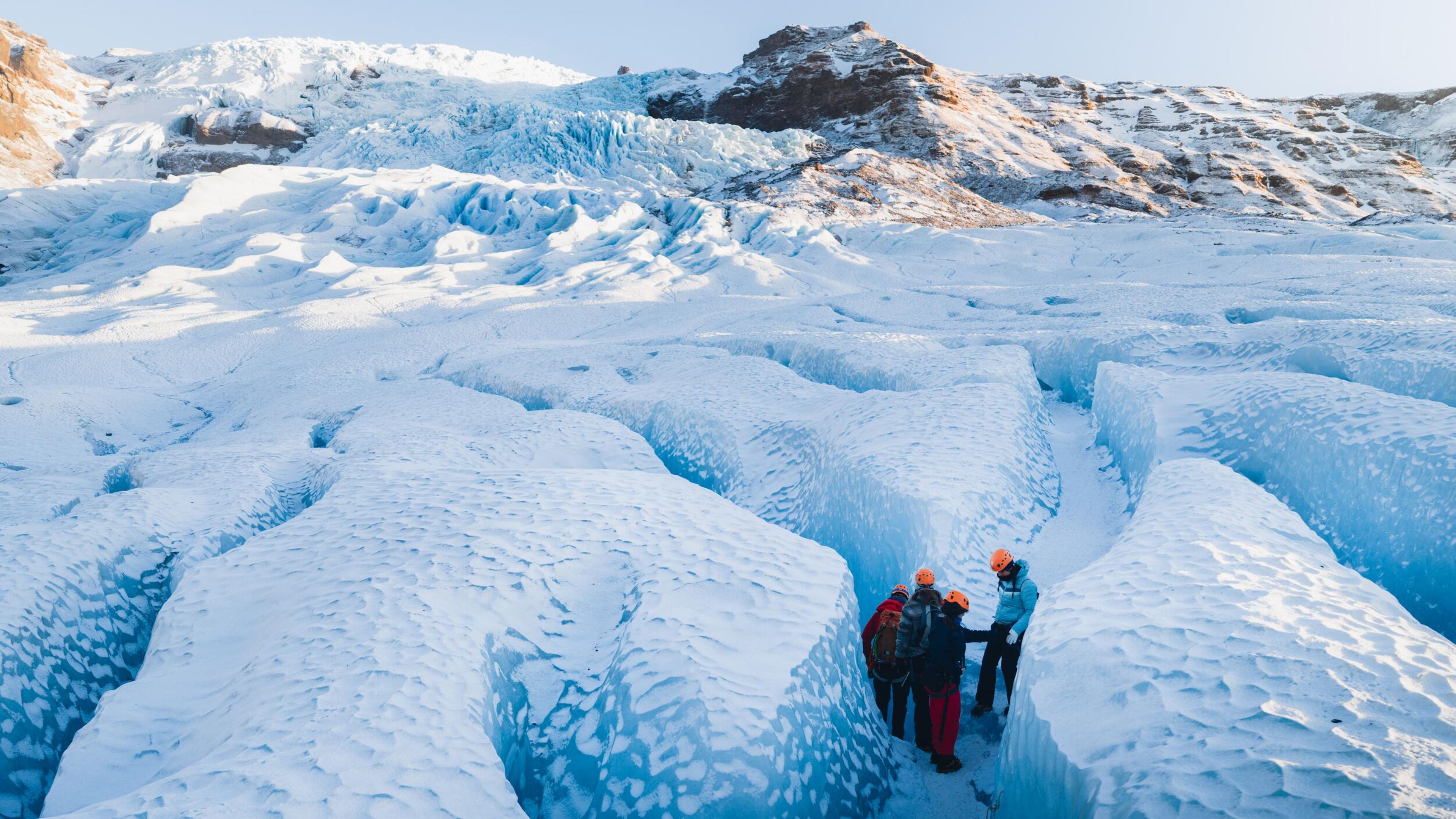 Four hikers in a small crevasse on the snow-covered blue ice of a glacier