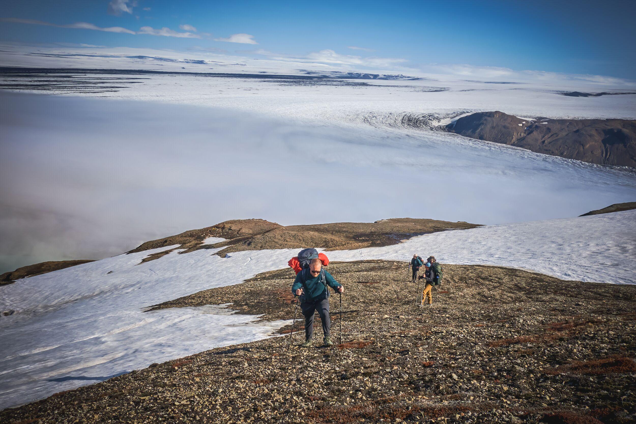 A man walking up a hill with a vast white glacier in the background