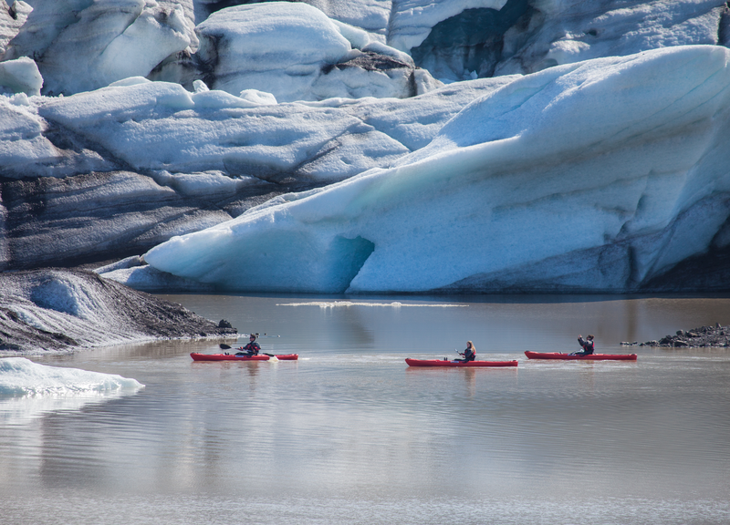 three people kayaking on a glacier lagoon by a glacier