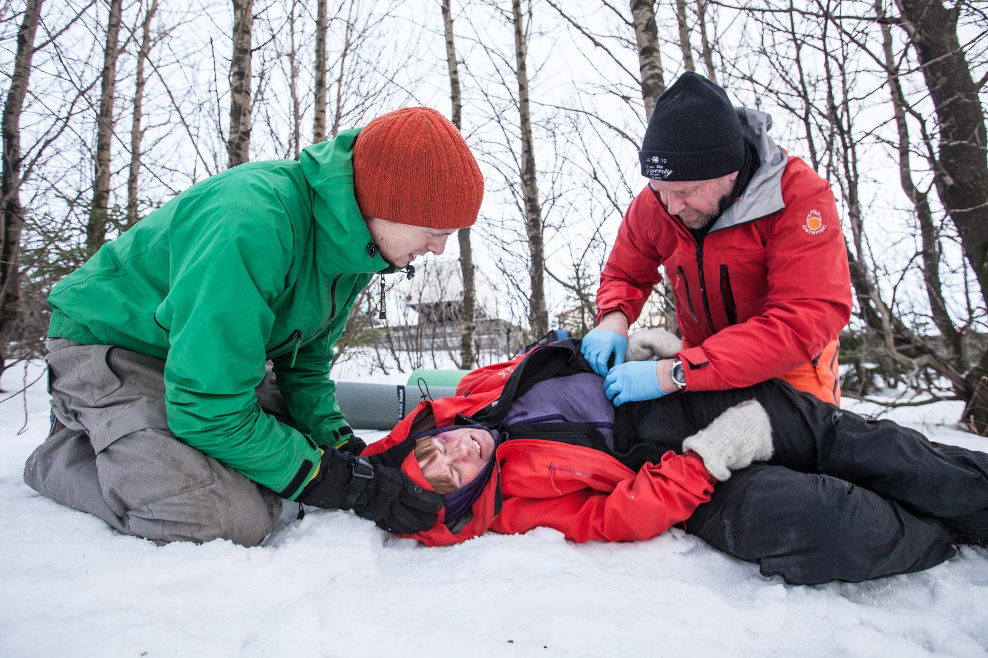 In this image, two individuals are administering first aid to a person lying on snow, simulating a winter rescue scenario.