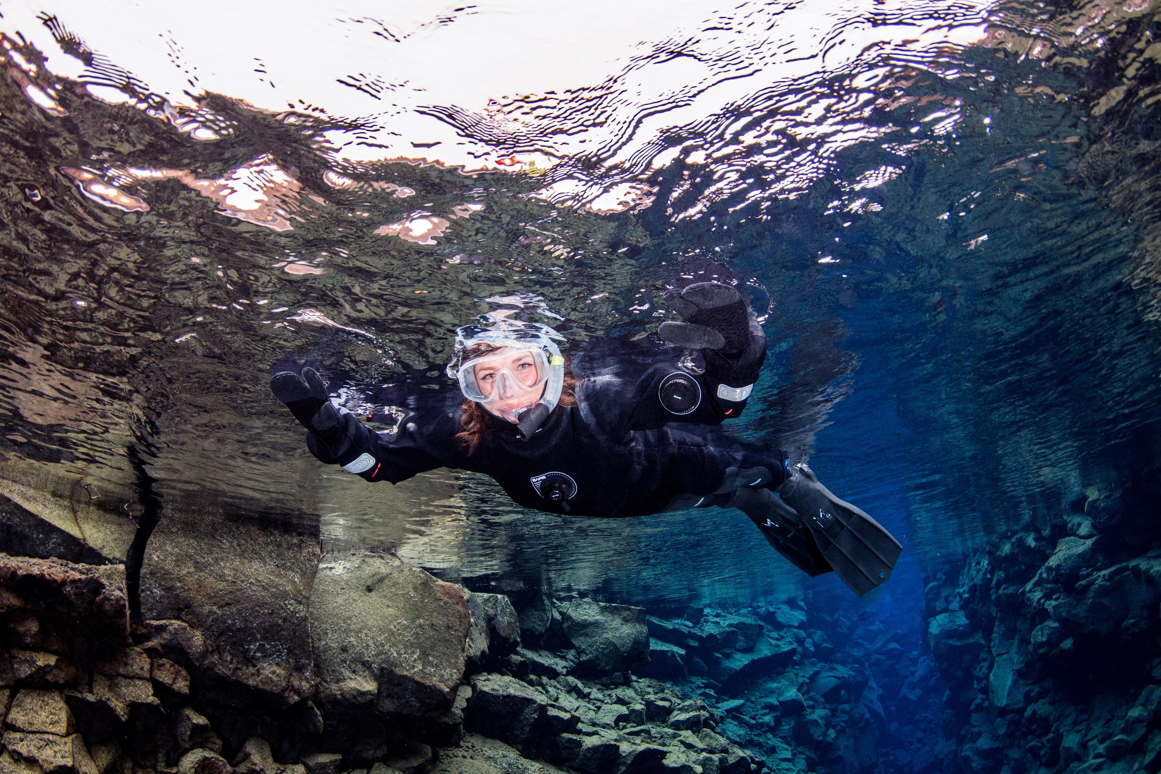 A woman in a dry suit looking at the camera while snorkeling in Silfra fissure.