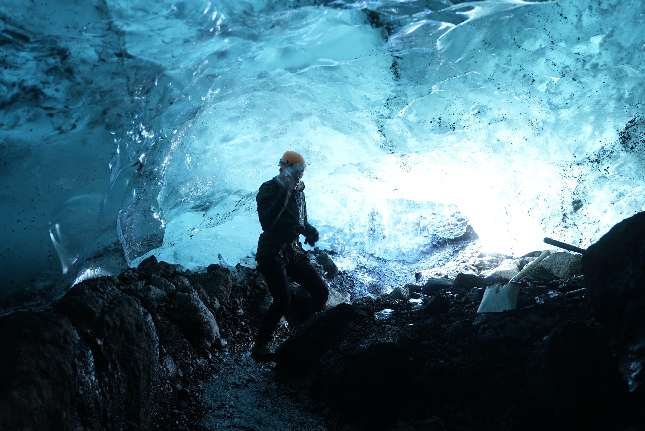 A person in a blue ice cave with a lot of light shining through the ice in the background