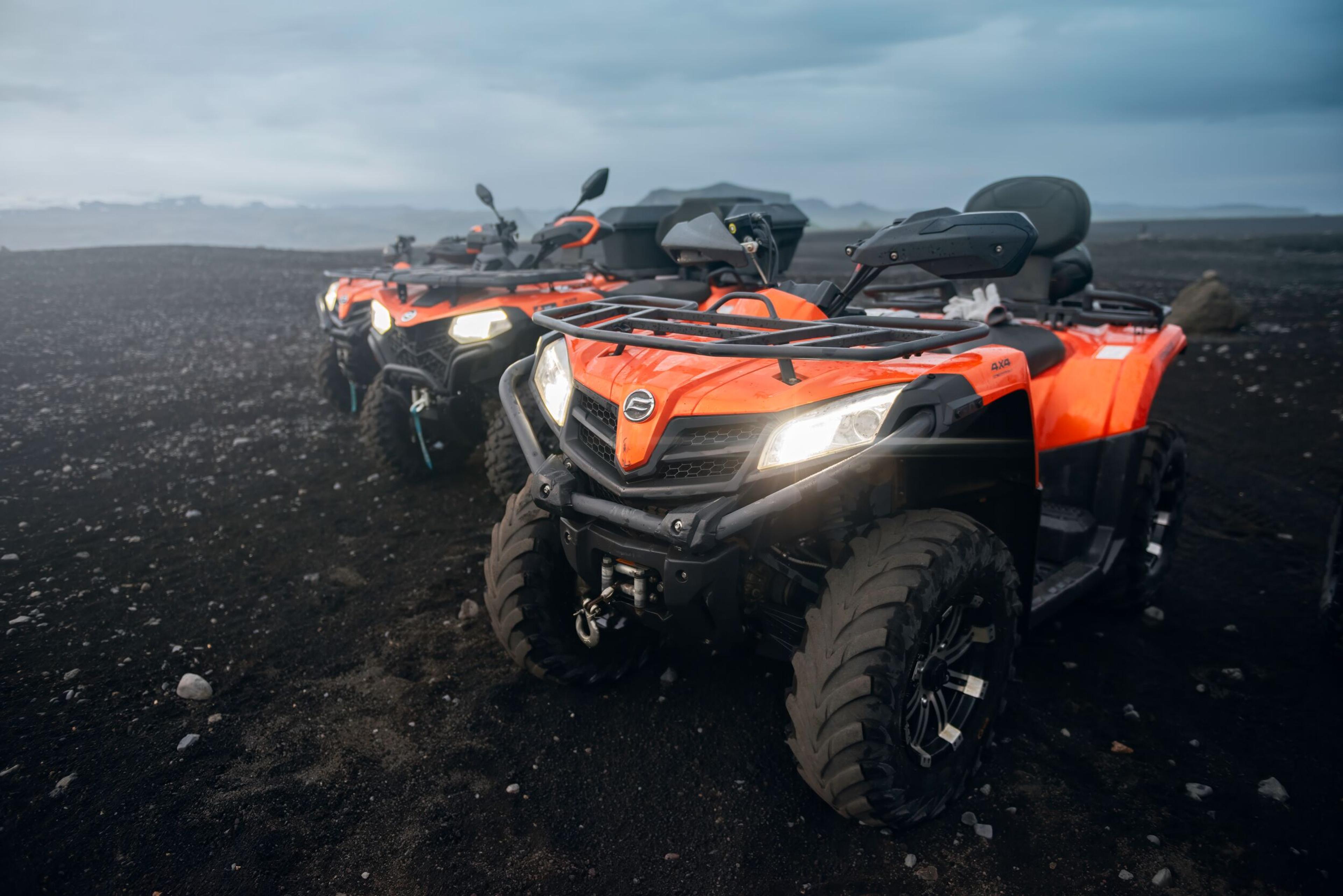 Close-up of a CFMOTO CFORCE 450 ATV with large tires, parked on black sand in Reykjavík, Iceland, with other ATVs visible in the background.