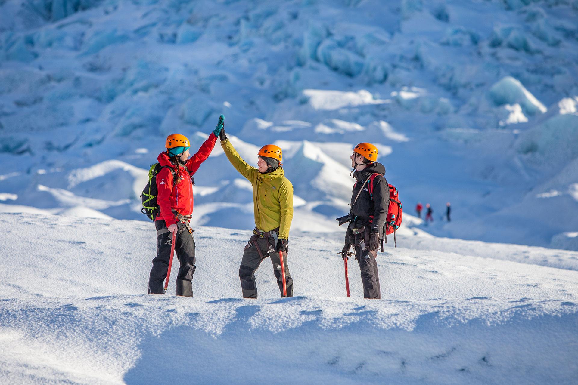 A female guide in a red jacket giving a high five to one of her clients on the Falljökull glacier hike