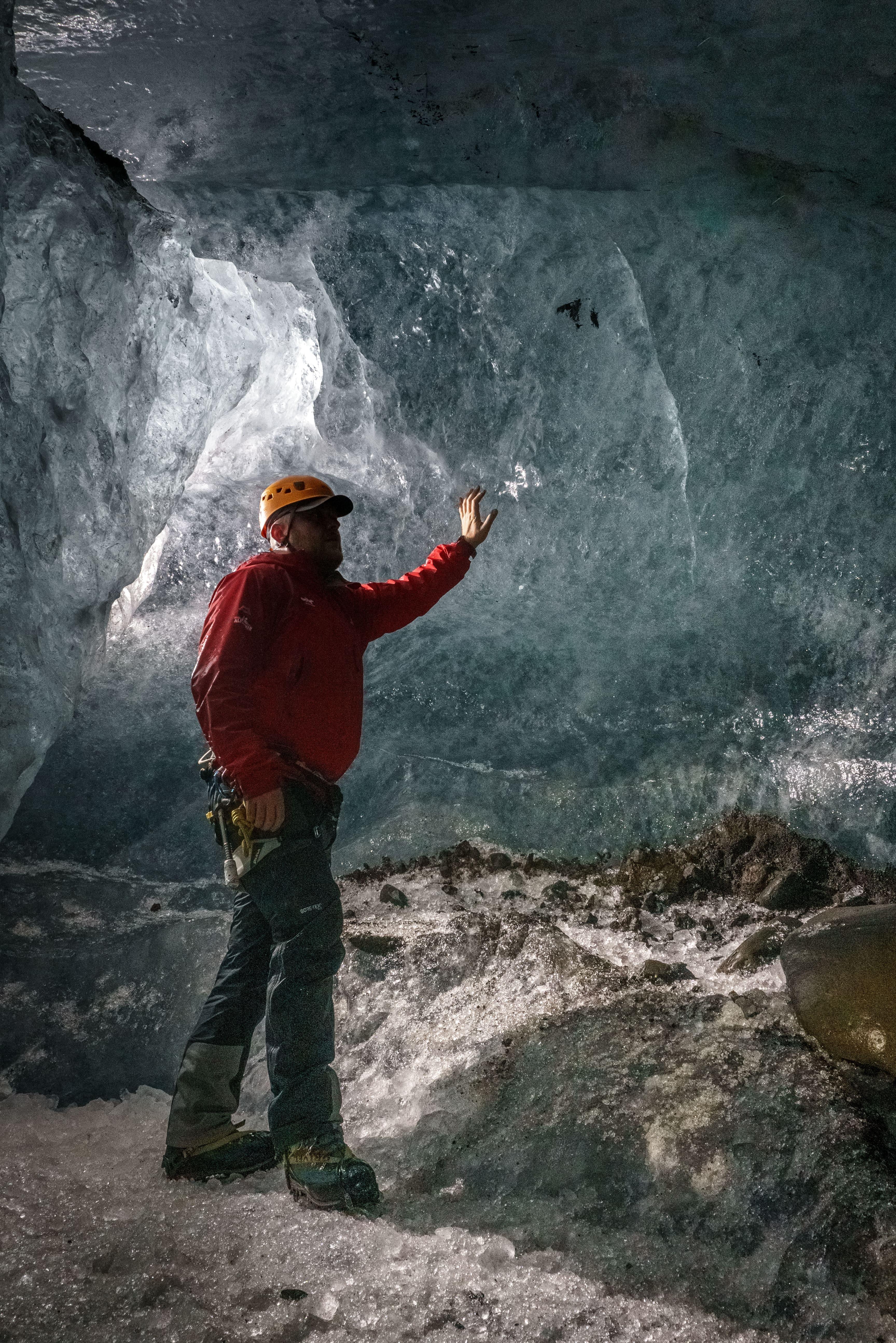 A glacier guide in red jacket touching an ice wall inside the ice cave.