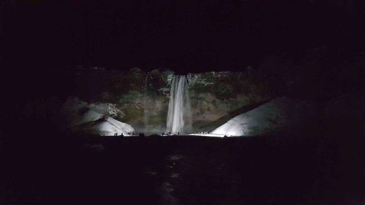 A picture of Seljalandsfoss in the night time with bright lights shining on the waterfall
