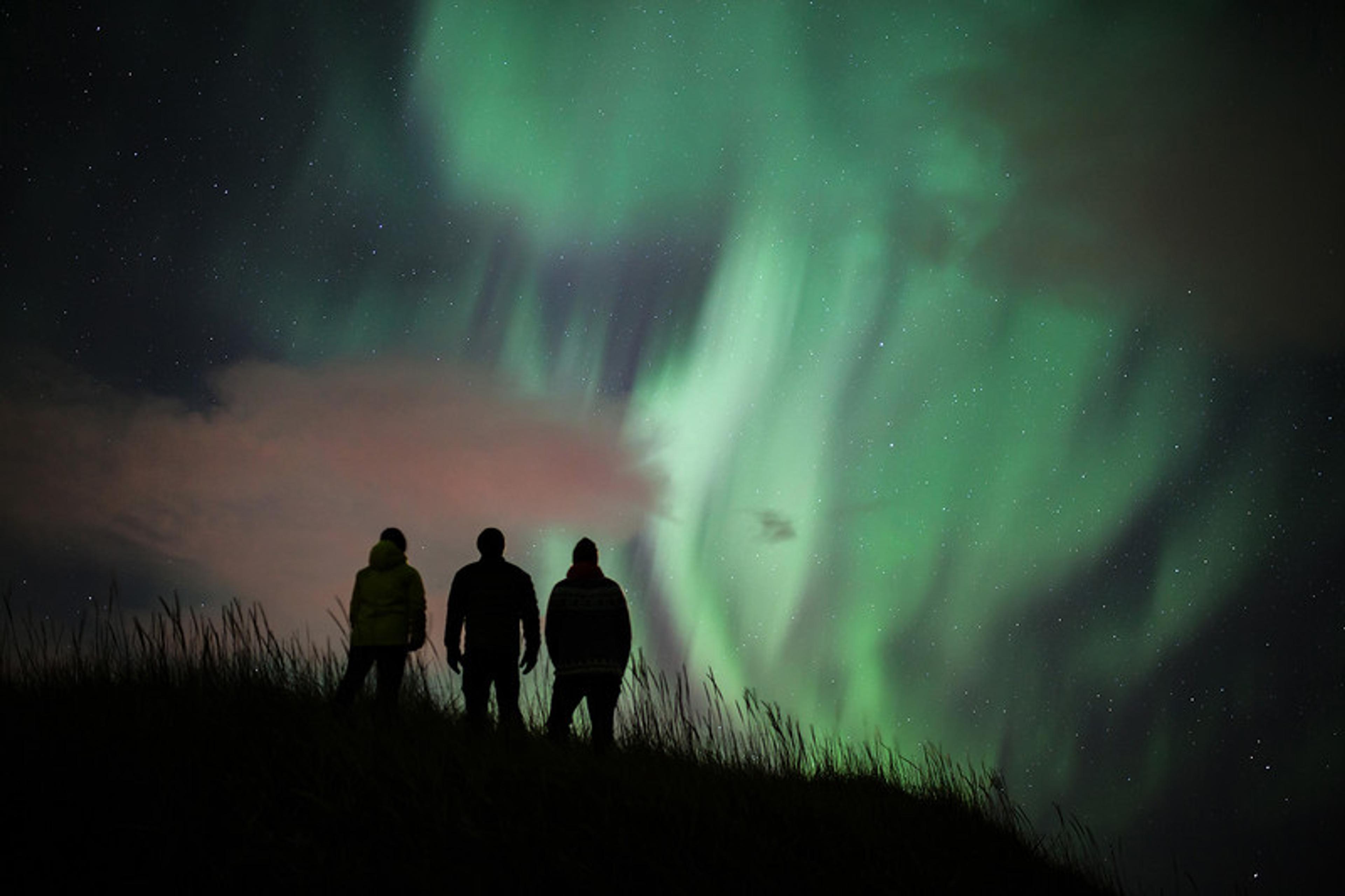 Three persons standing and admiring the dance of the northern lights