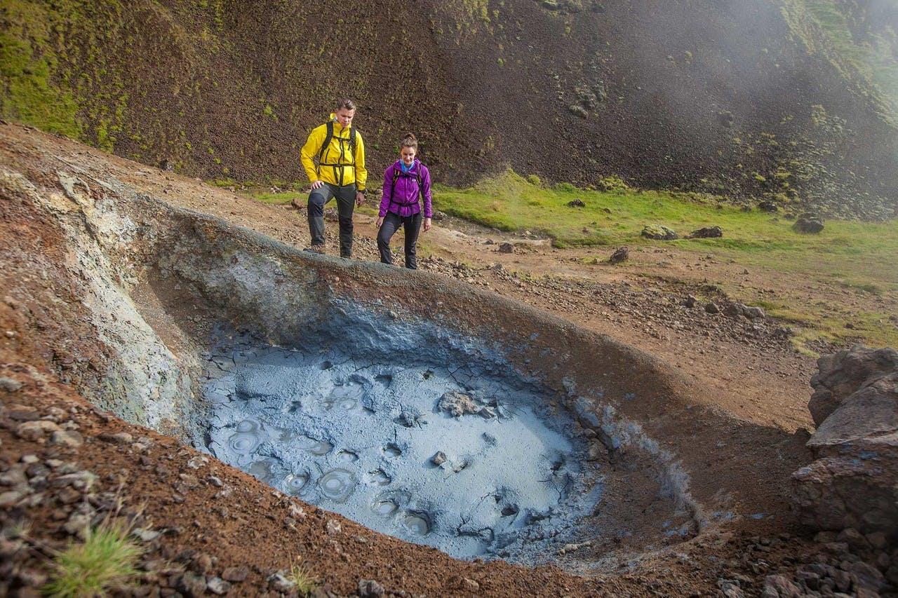 A couple hiking near a muddy hot spring in Iceland