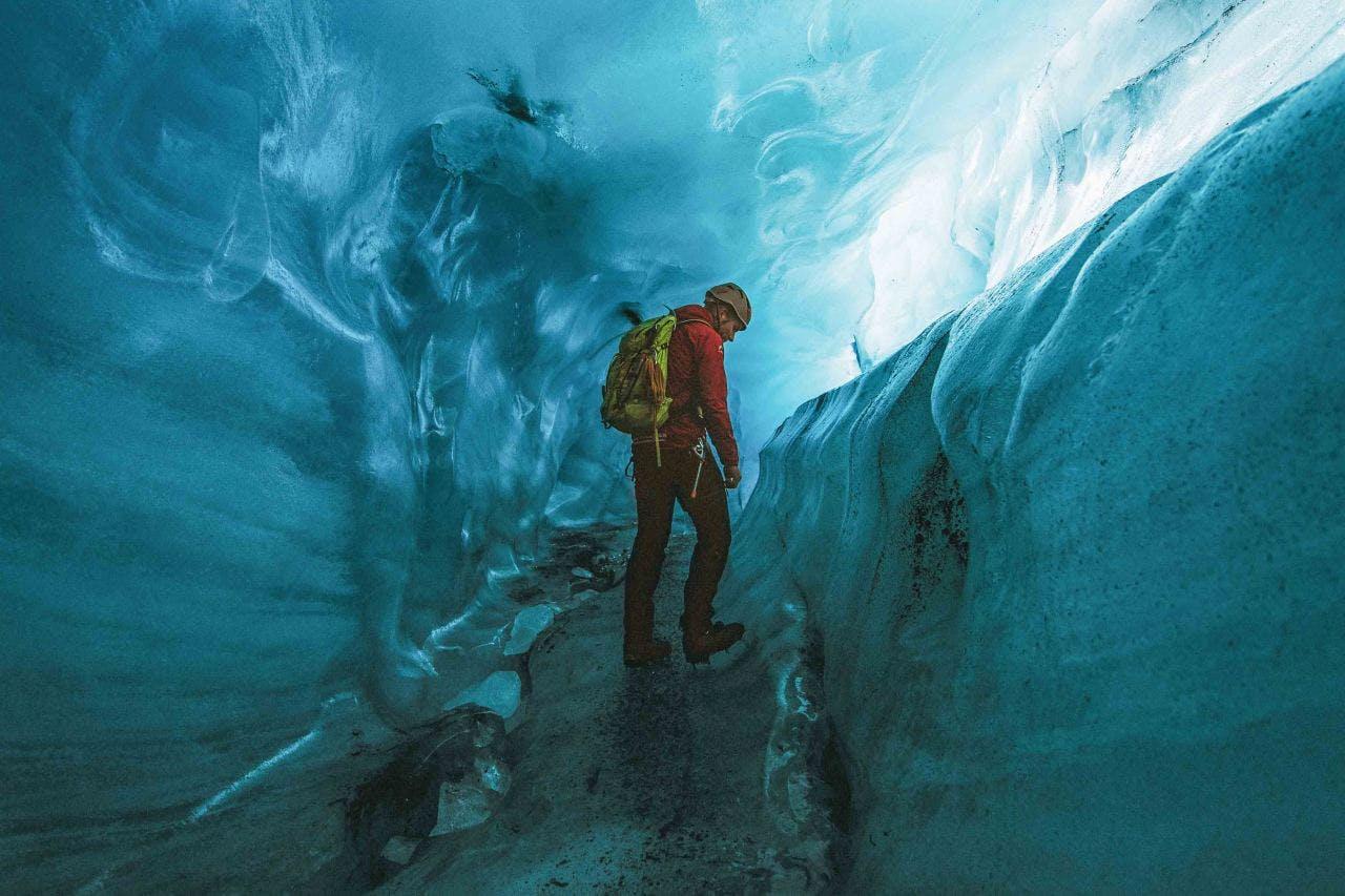 man wearing a red jacket and a yellow helmet standing in an ice cave