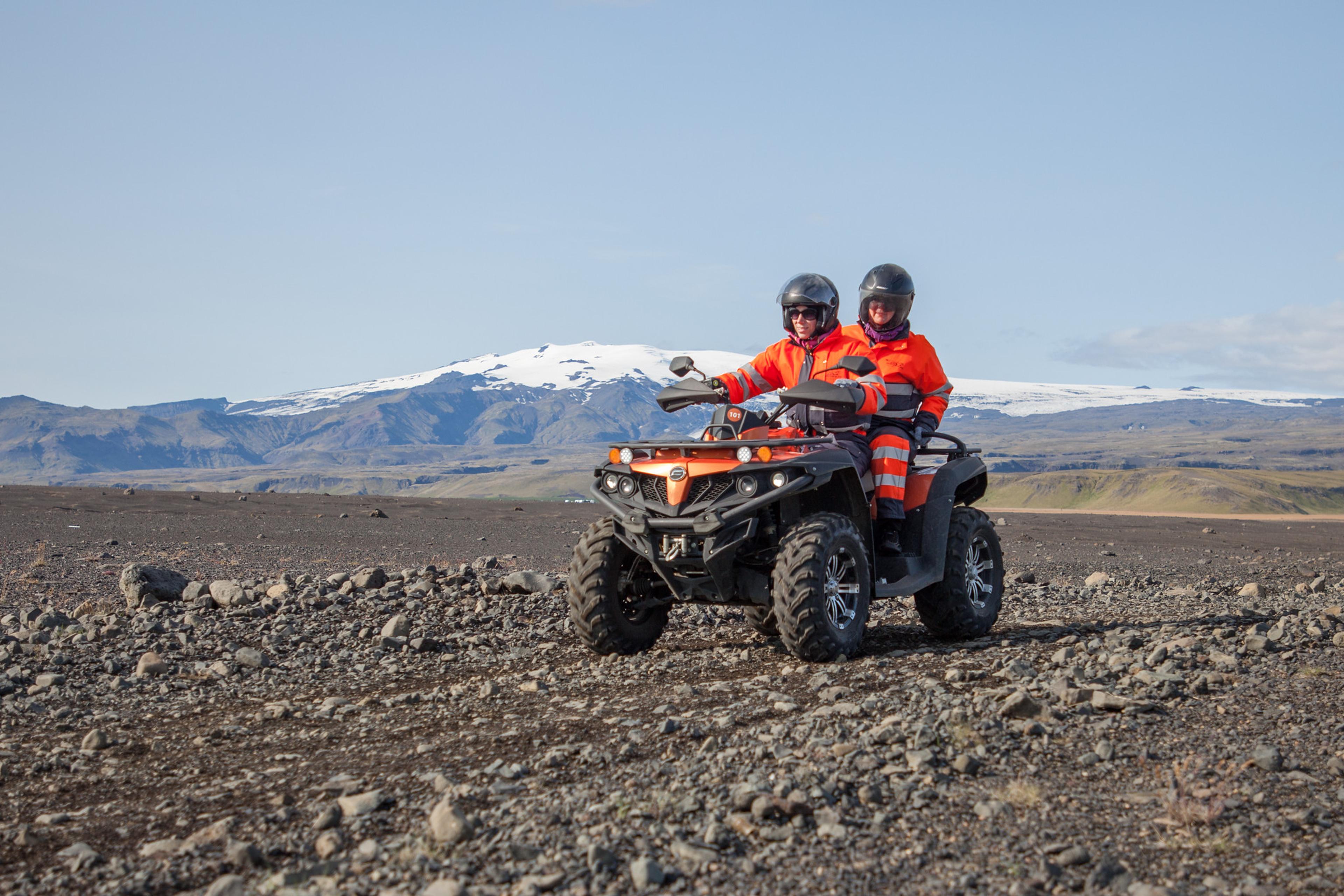 A couple on a ATV quad bike riding on the black sand area of Sólheimasandur