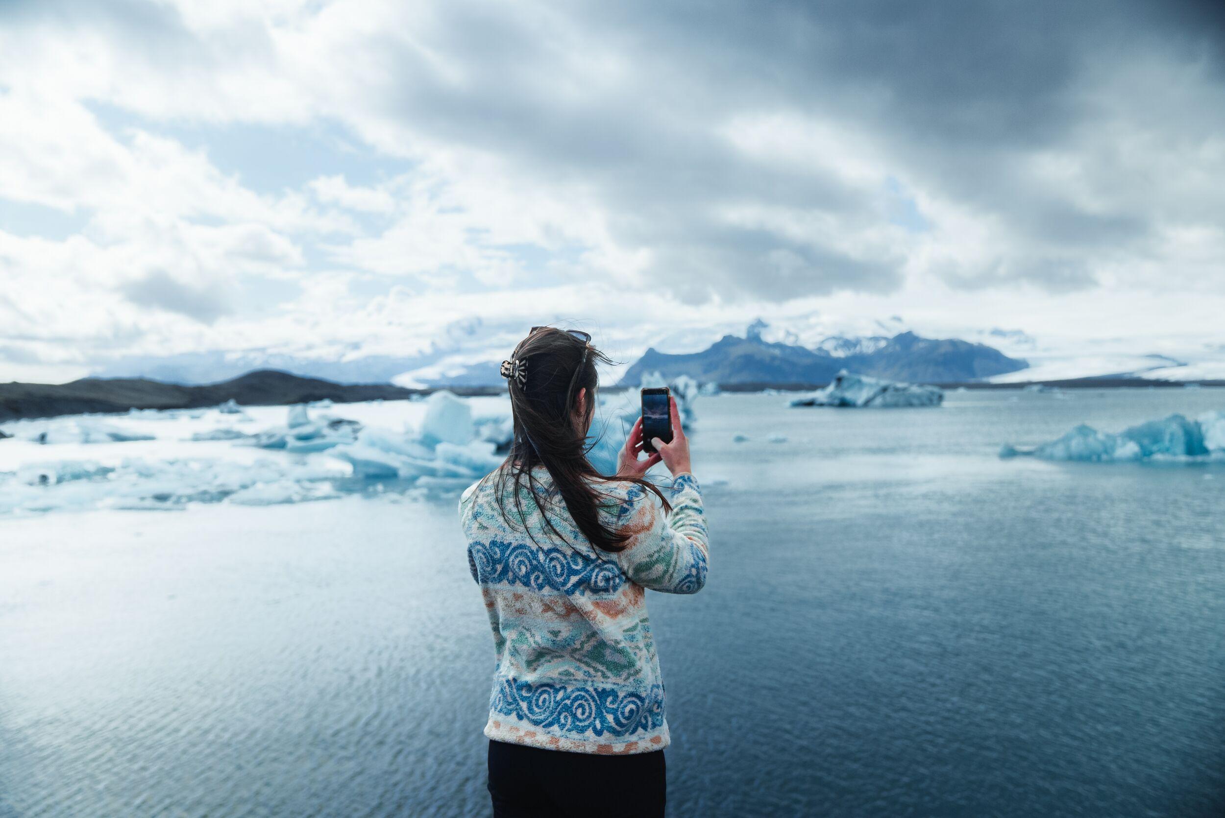 Womand taking a photo on a phone of a glacier lagoon