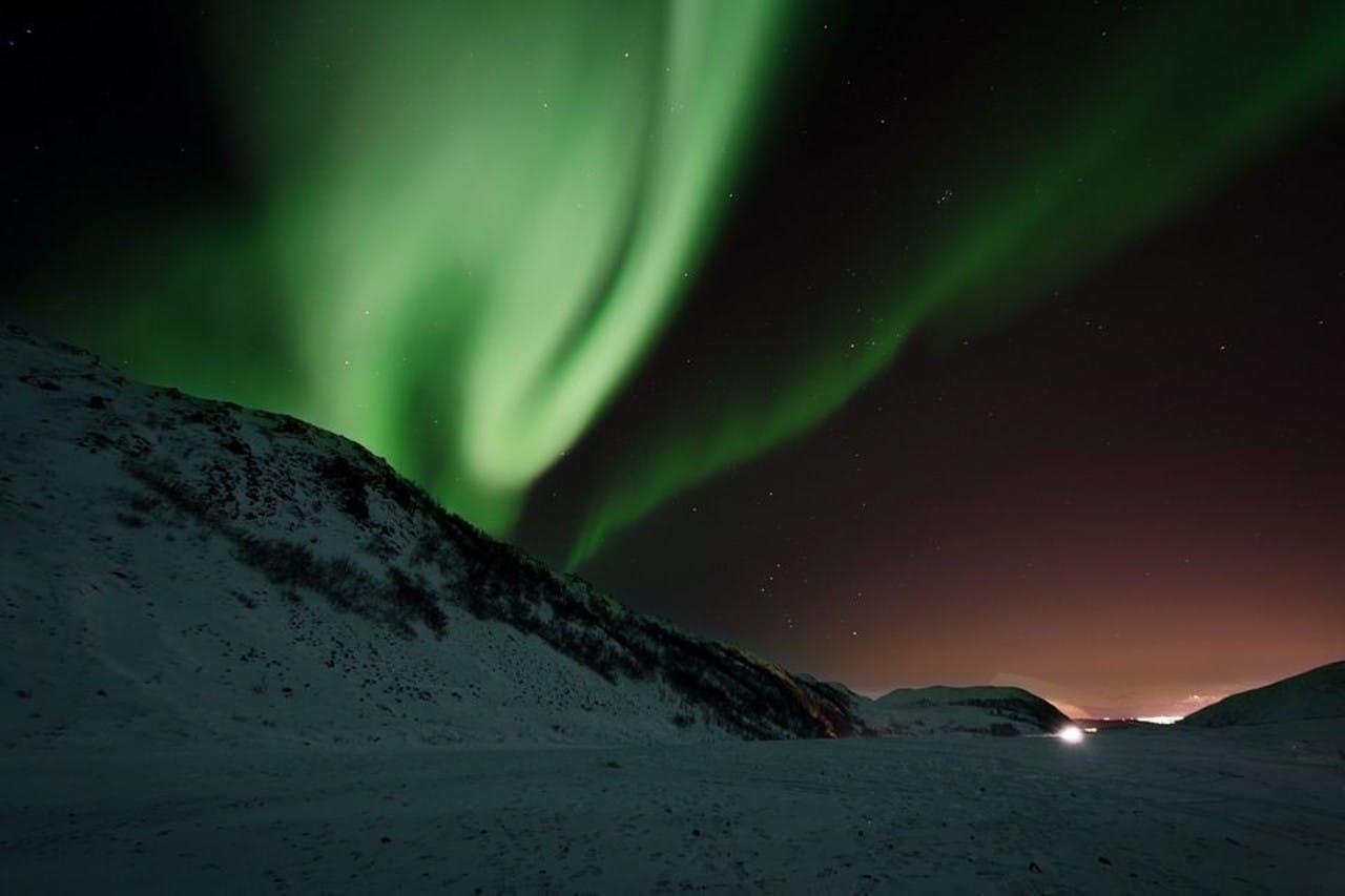 Green Iceland Northern Lights (Aurora Borealis) dancing in a dark sky above a snowy hill