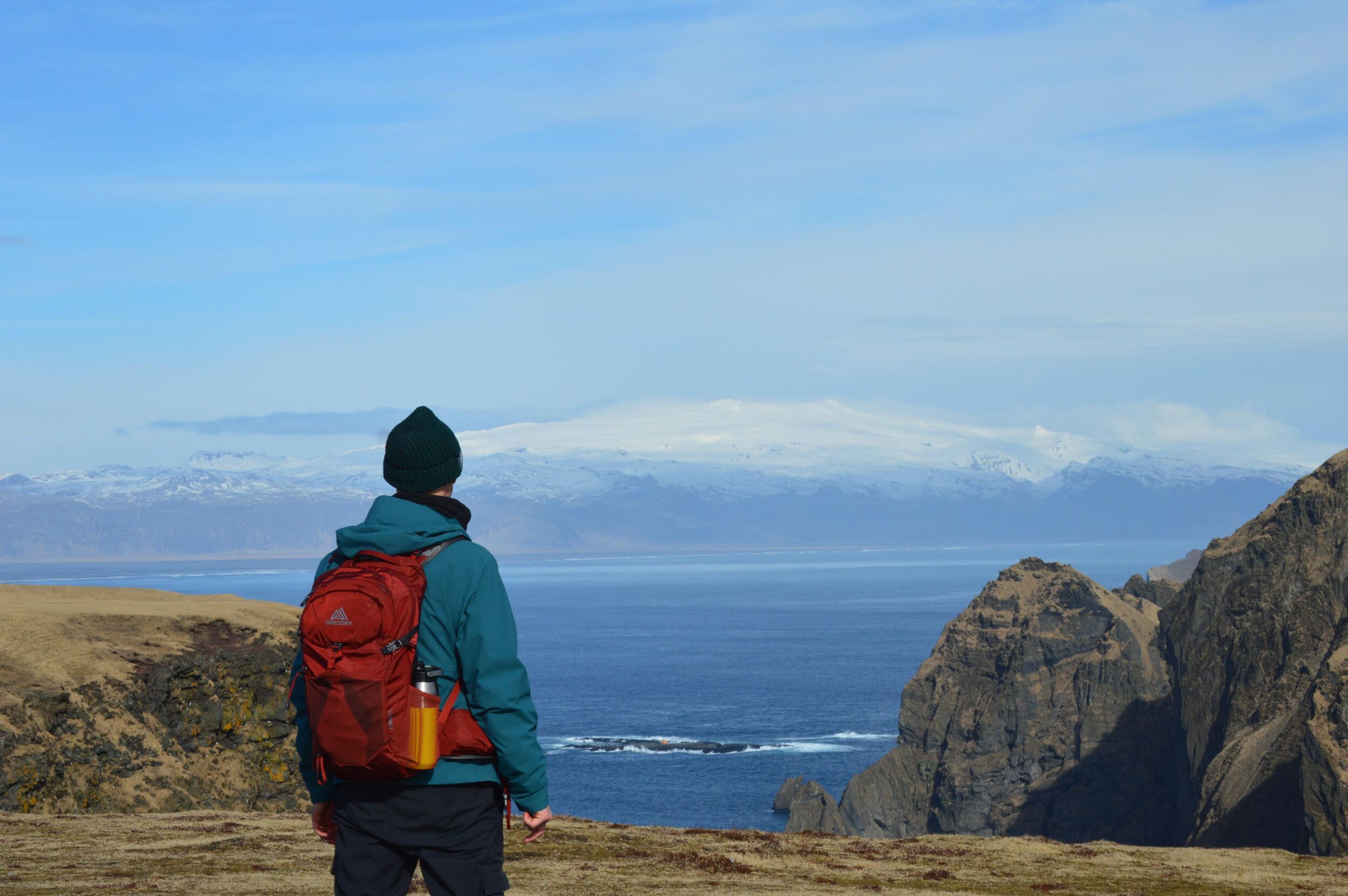 A woman hiker standing on a hill with a backpack looking over the sea at Eyjafjallajökull in the distance