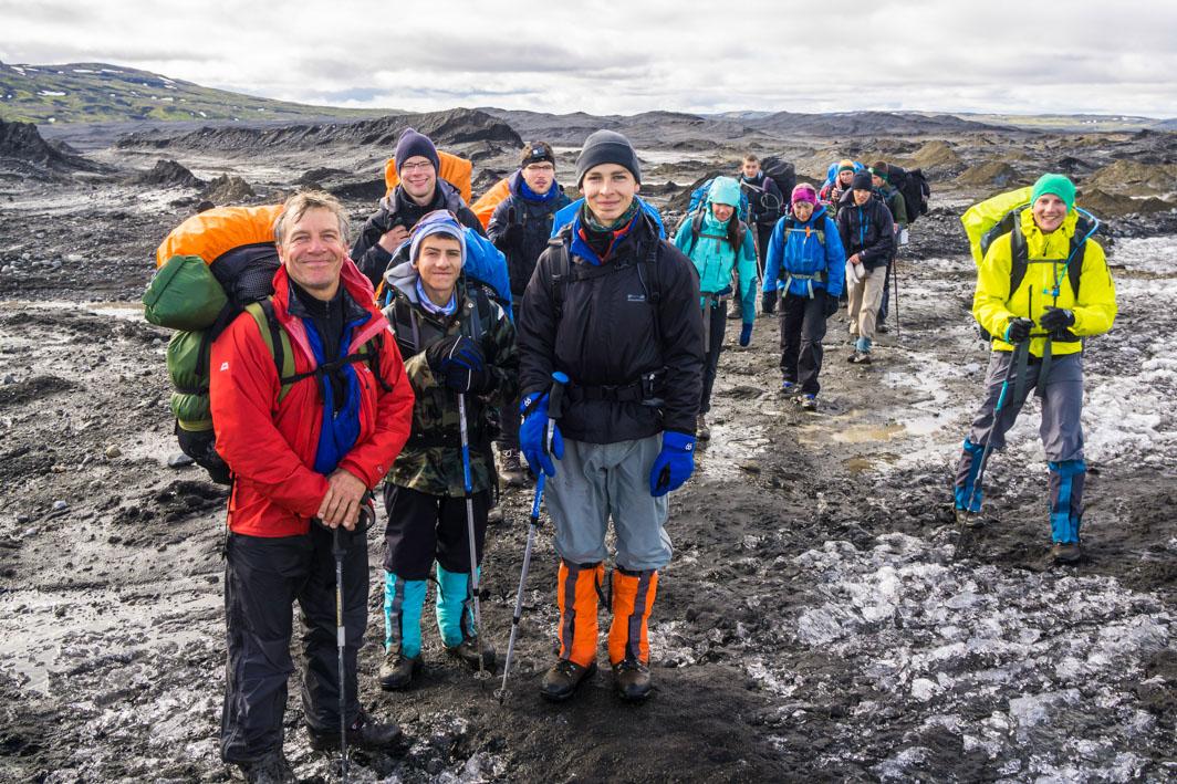 A group of hikers, equipped with backpacks and trekking poles, traverses a rugged volcanic terrain in Iceland.