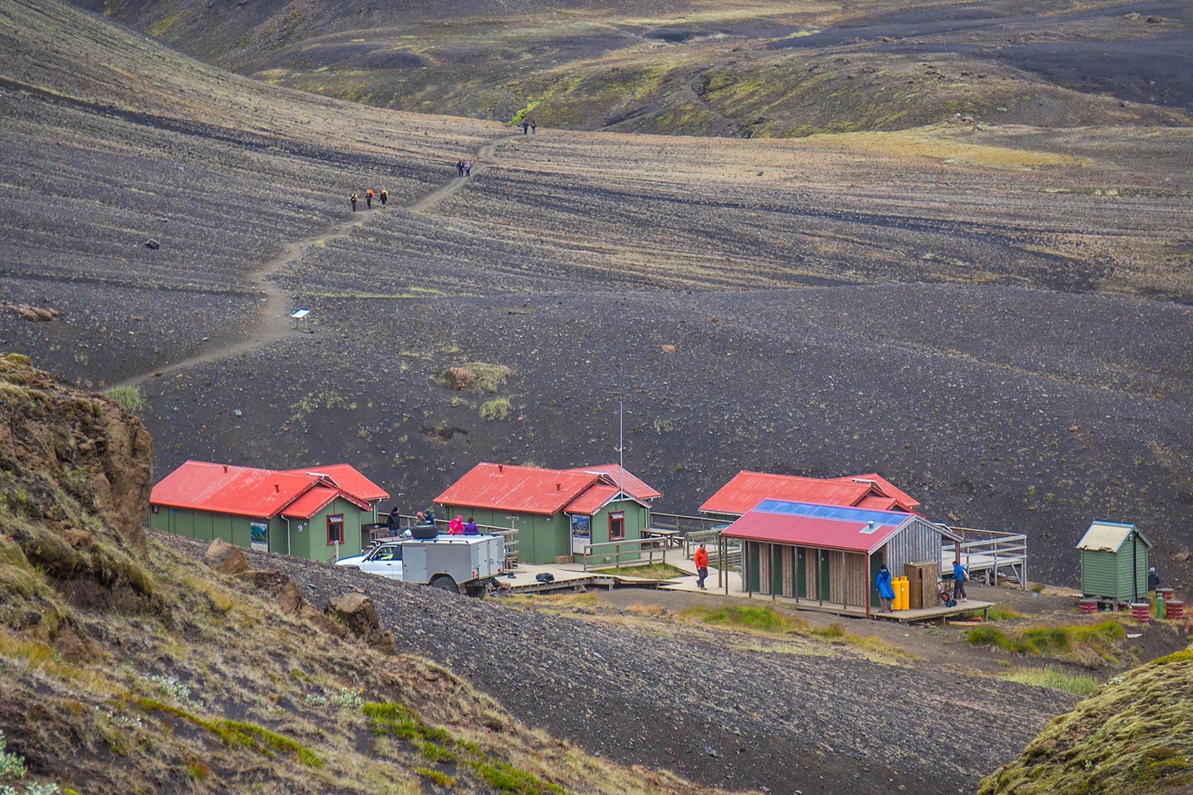 A road leading to the cliffs covered in moss behind a few red roofed huts