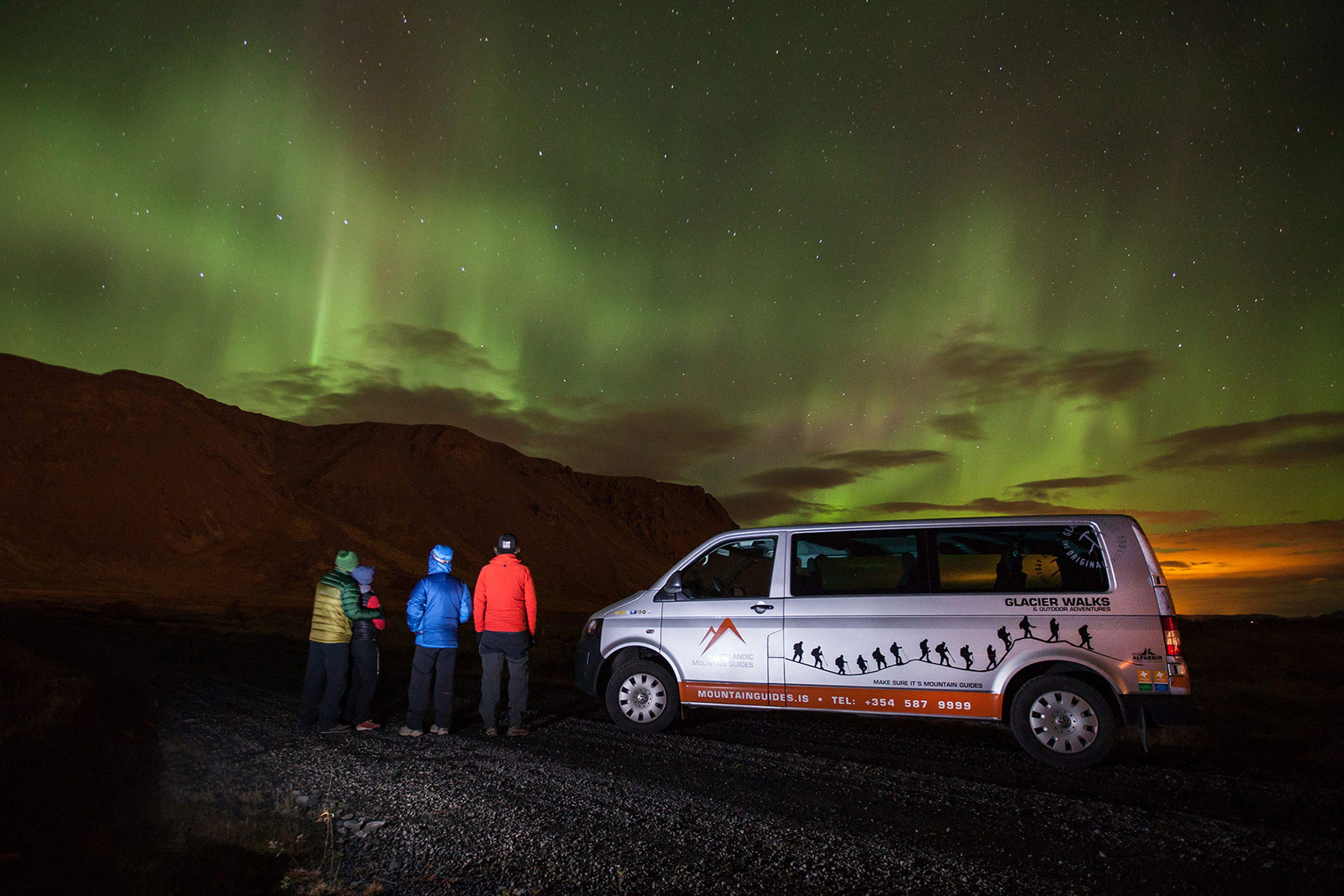 People next to a car enjoying the green northern lights
