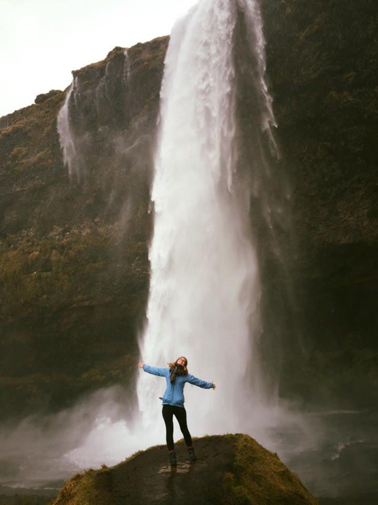 Happy woman in blue standing in front of Seljalandsfoss waterfall in Iceland