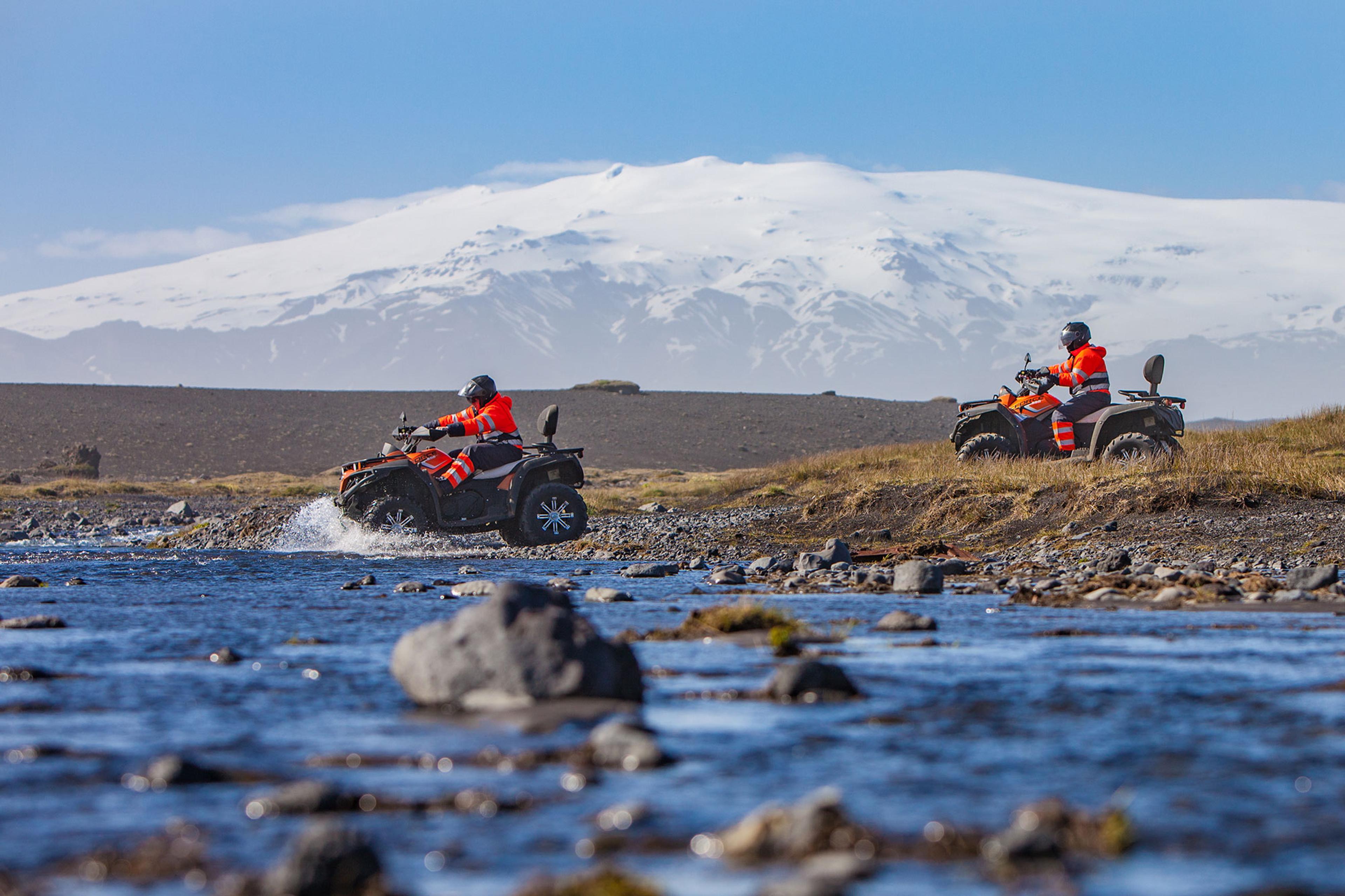 People on ATV quad bike scorssing a big river and the glacier in the background