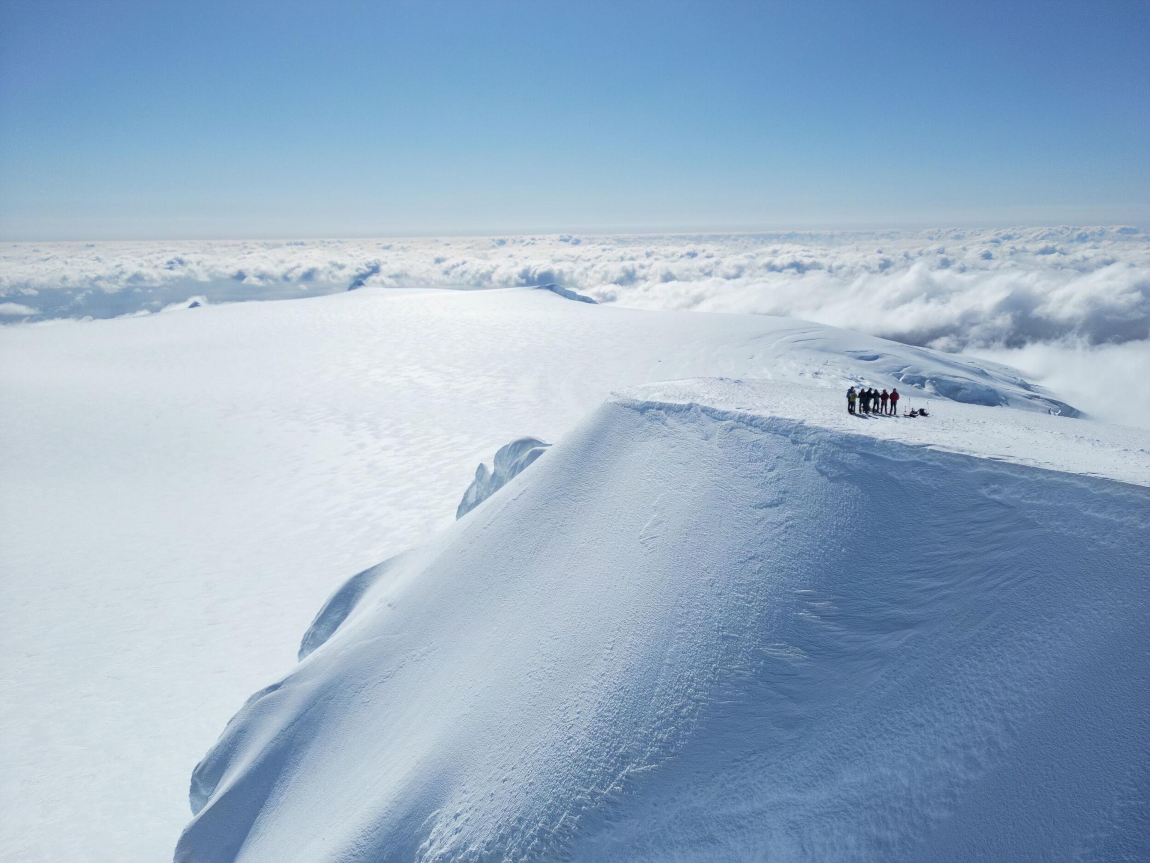 Hikers at the top of Hvannadalshnúkur, above the clouds with blue skies in the background