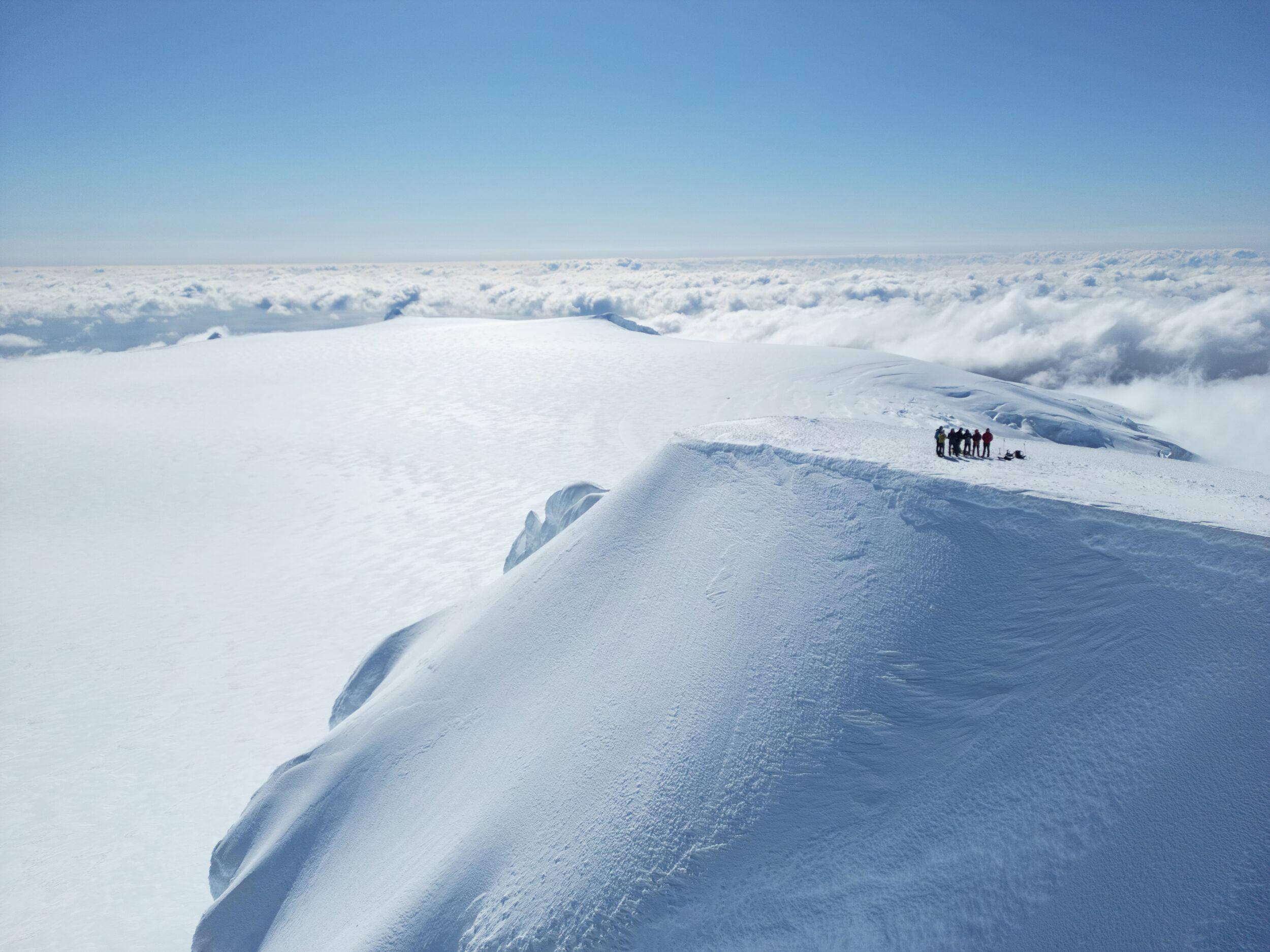 Hikers at the top of Hvannadalshnúkur, above the clouds with blue skies in the background