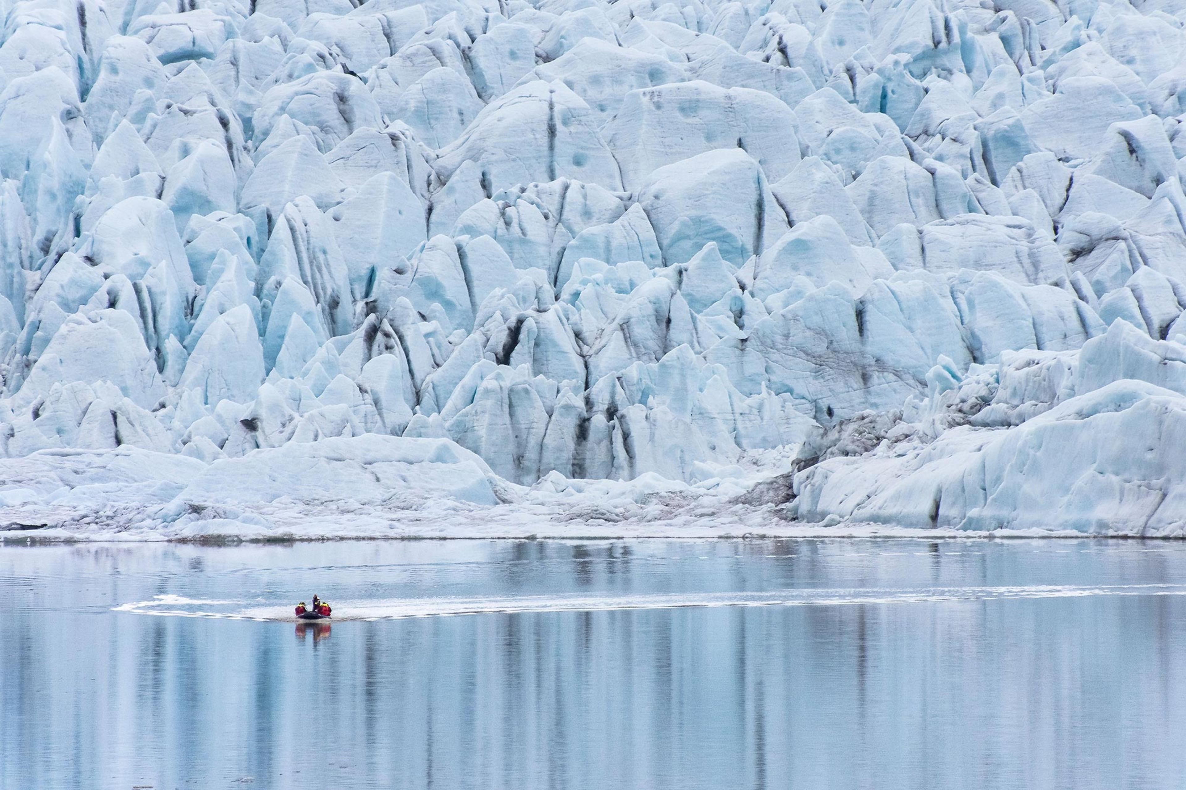 A small boat on a calm iceberg lagoon with a stunning glacier behind it.
